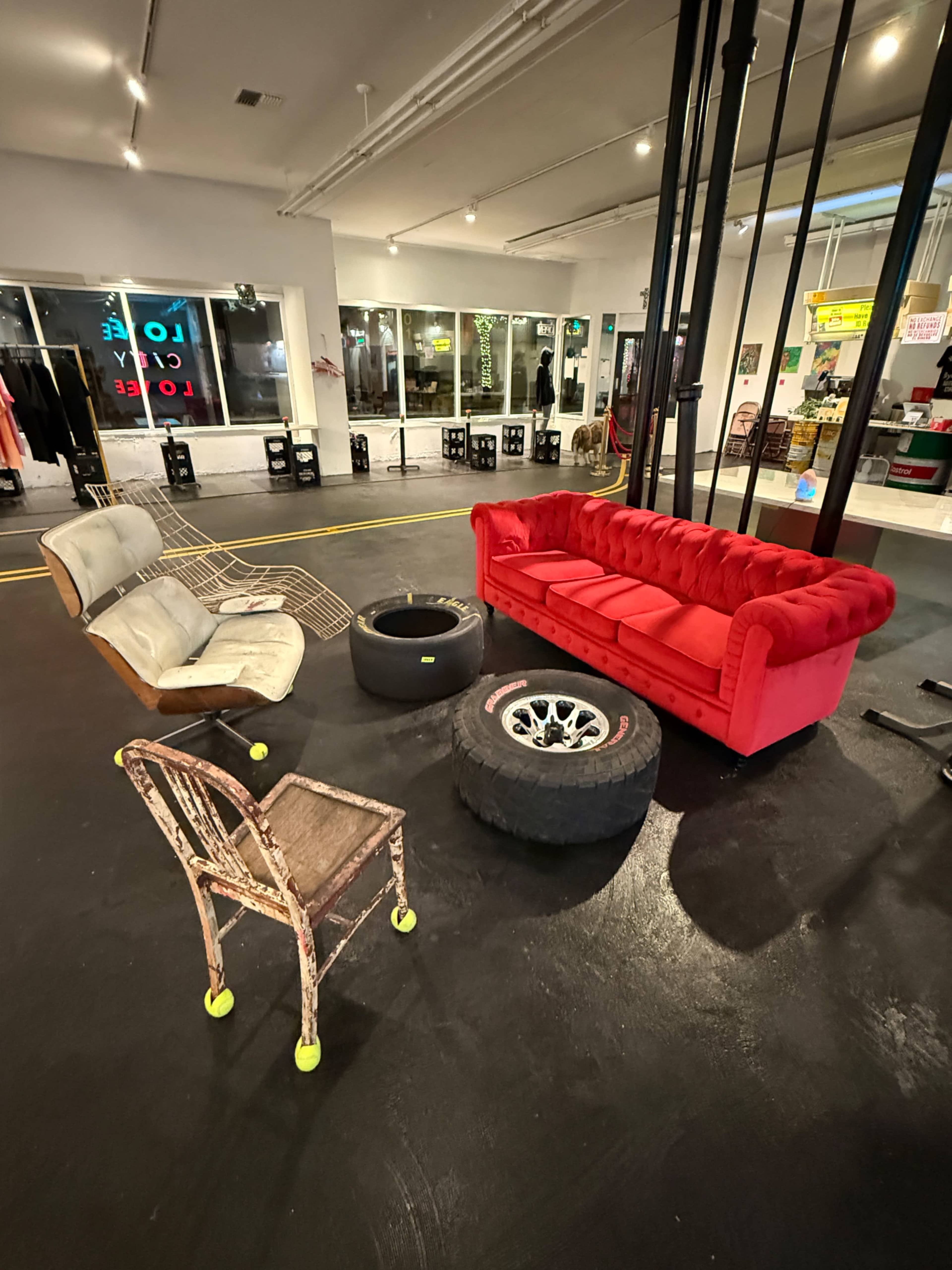 The image shows a red couch, a wireframe chair, a tire, and a car wheel arranged on a black floor in a well-lit interior space.