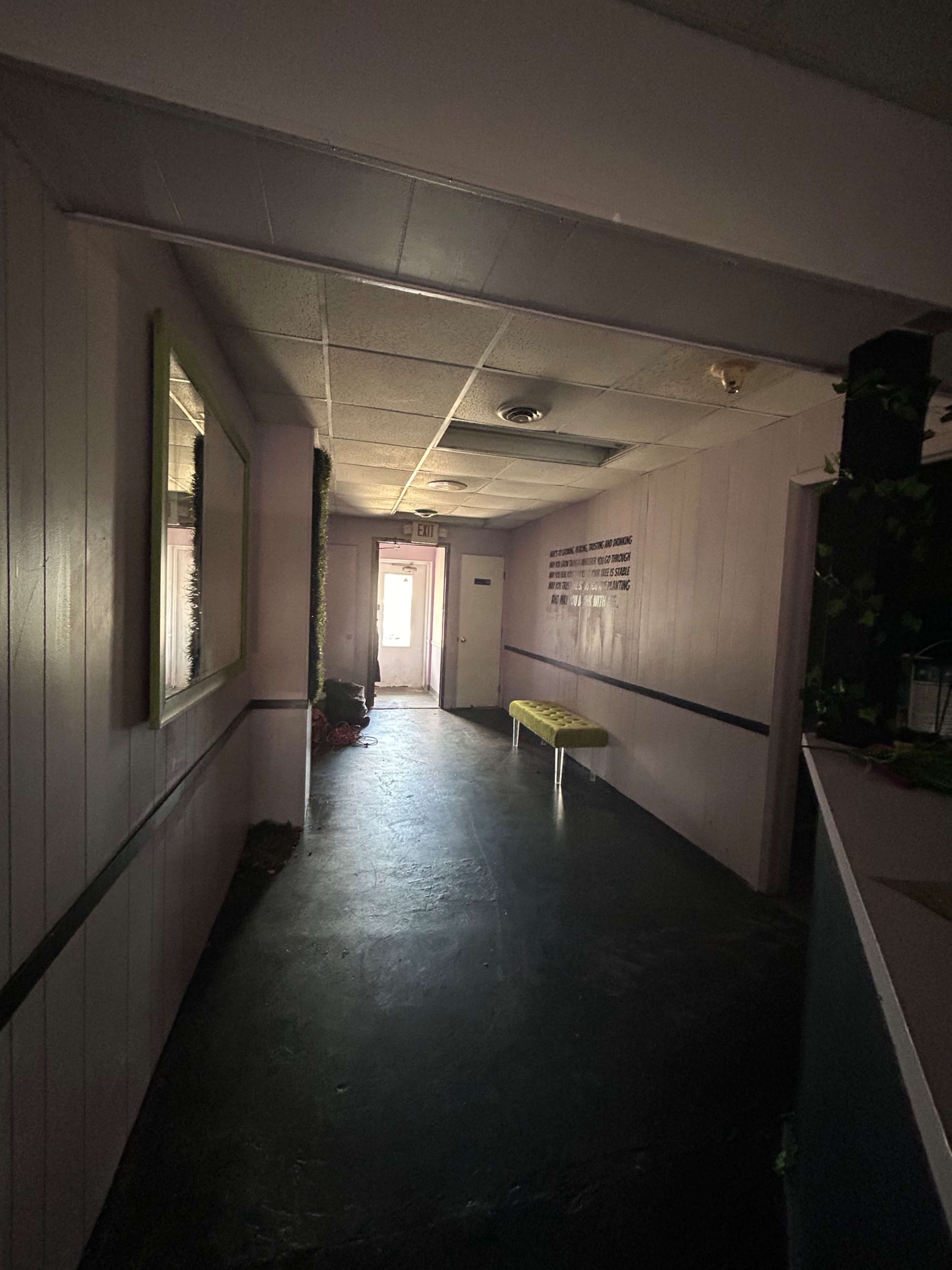 A dimly lit hallway features a bench along one wall and a doorway at the end leading outside.