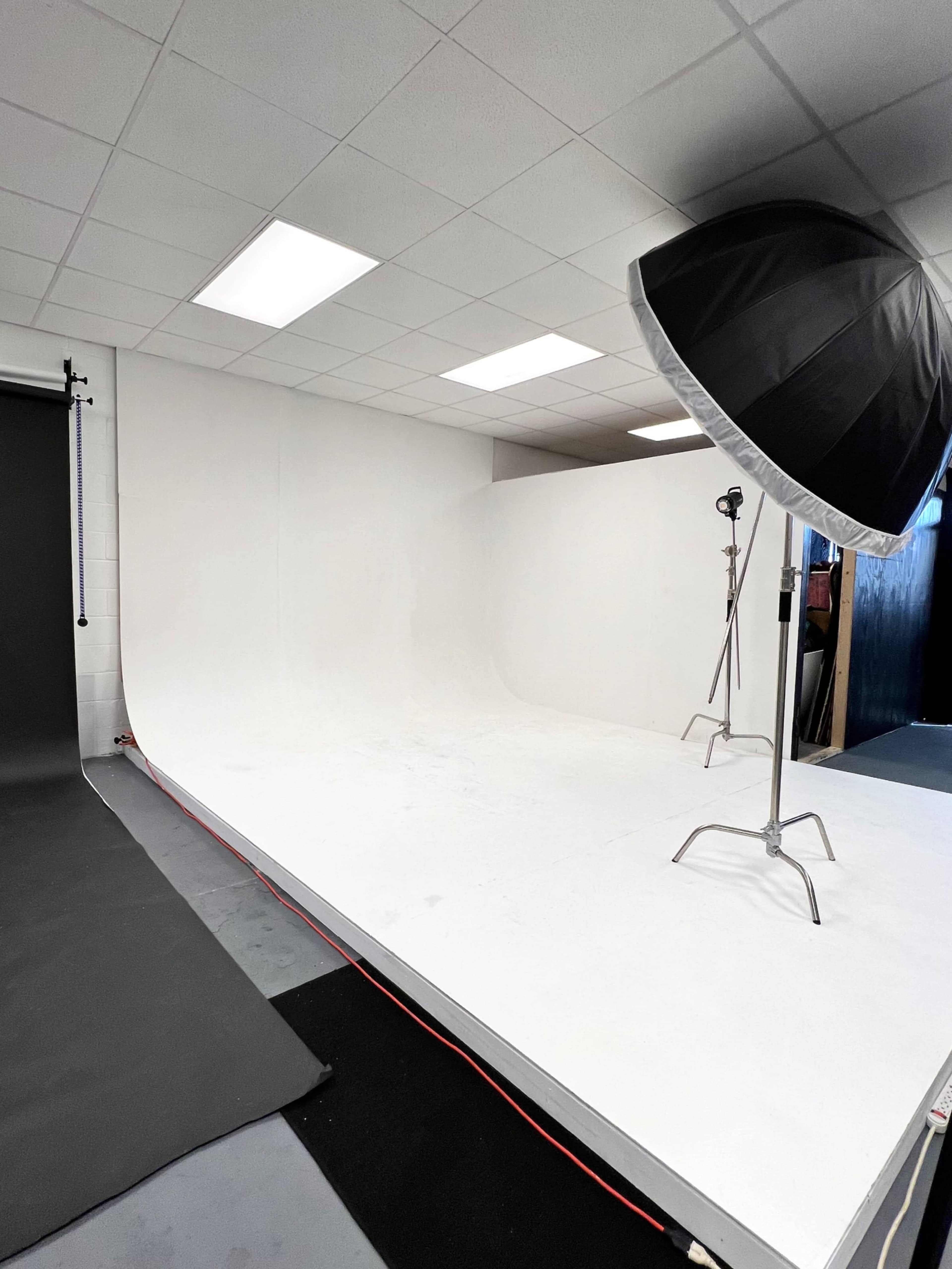 A photography studio with a white backdrop, softbox lighting, and a dark floor mat.