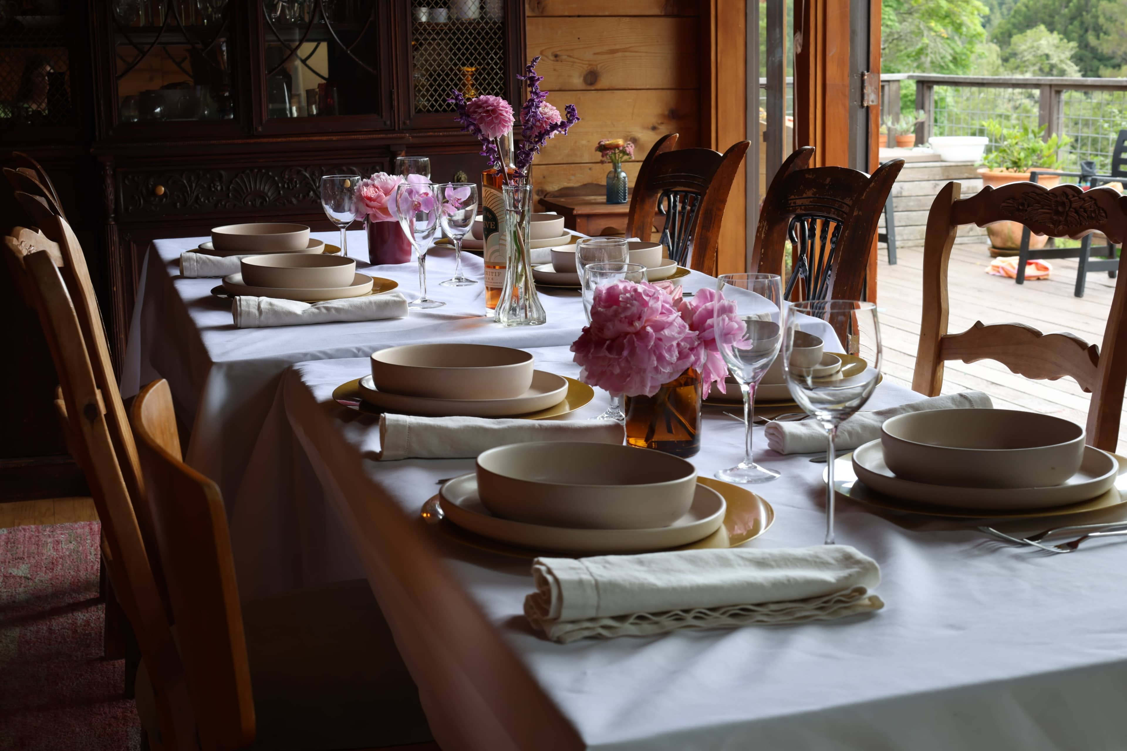 A long dining table is set with elegant dishes, glassware, and floral centerpieces in a rustic wooden setting.