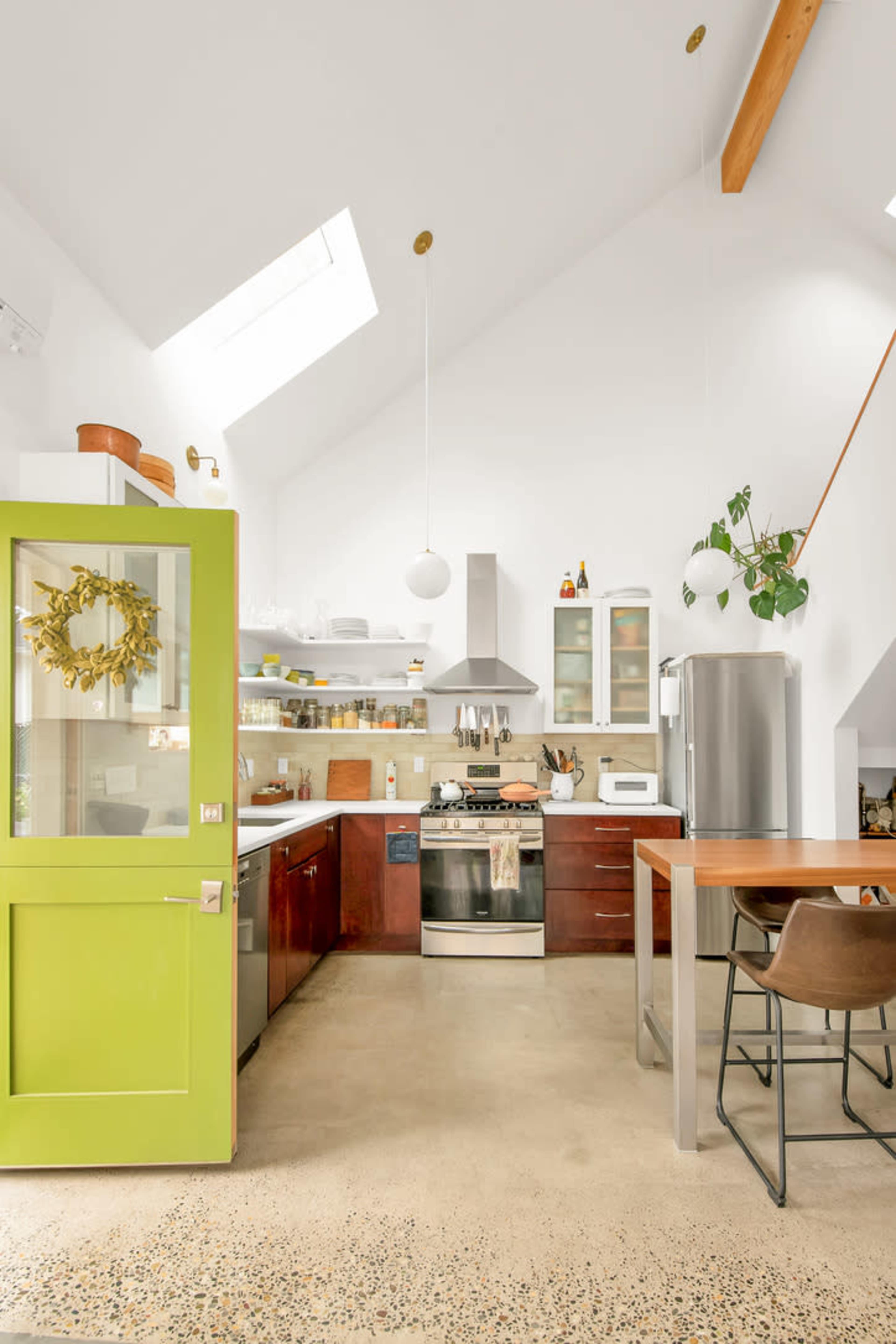 A modern kitchen features green cabinetry, stainless steel appliances, and a skylight illuminating the space.