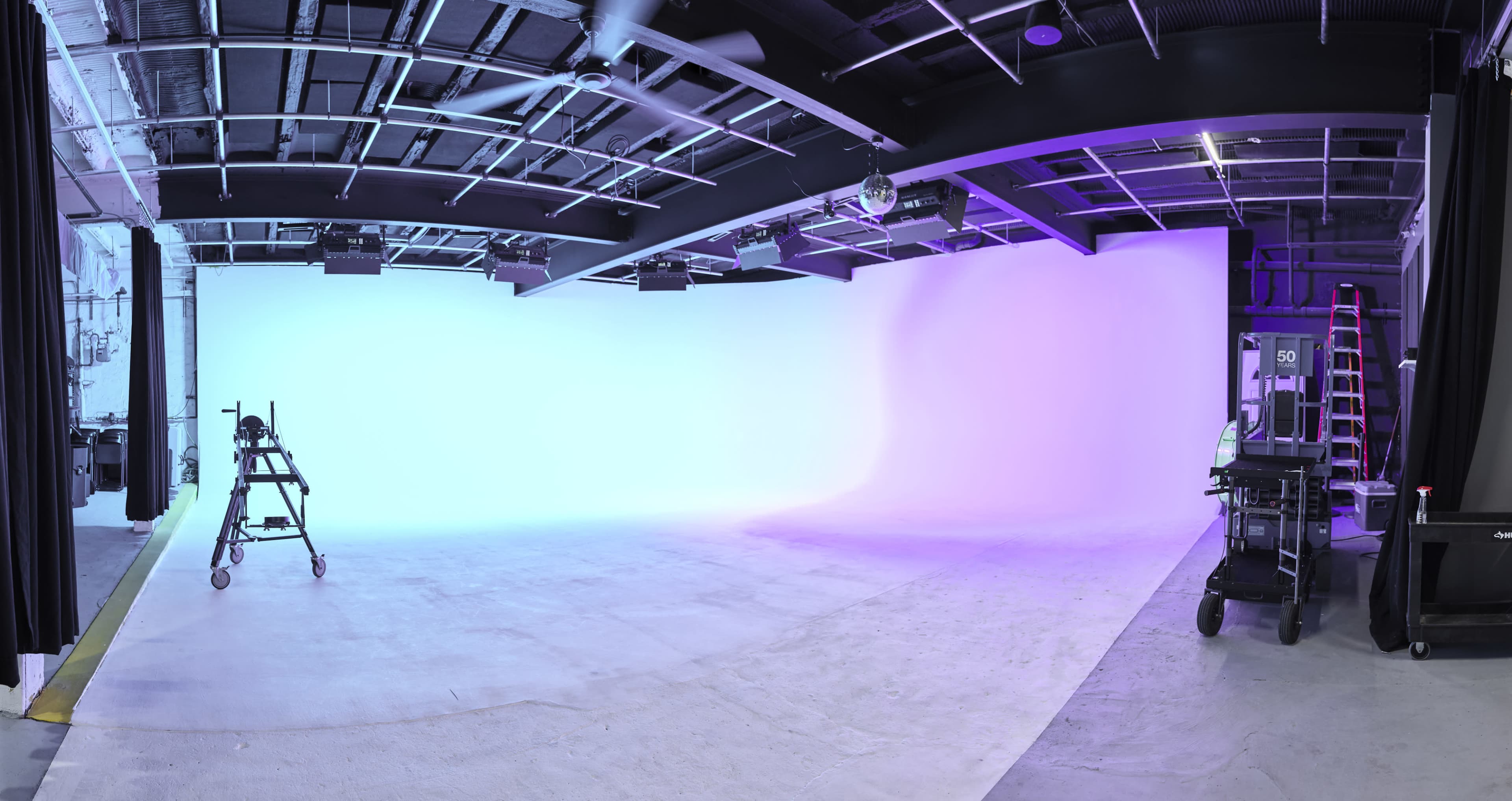A spacious photography studio with a gradient backdrop and various equipment set up around the room.