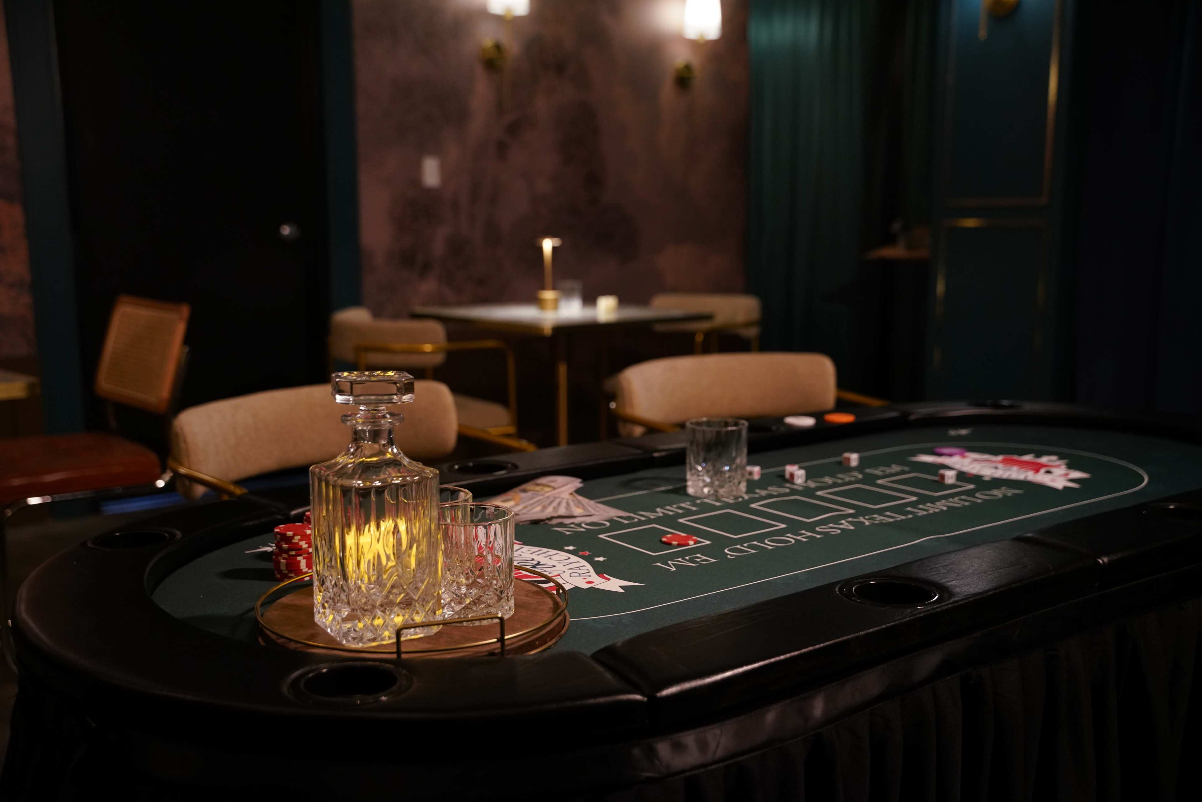 The image shows a well-set gambling table with a green felt surface, featuring a decanter and glasses beside poker chips and a tray.