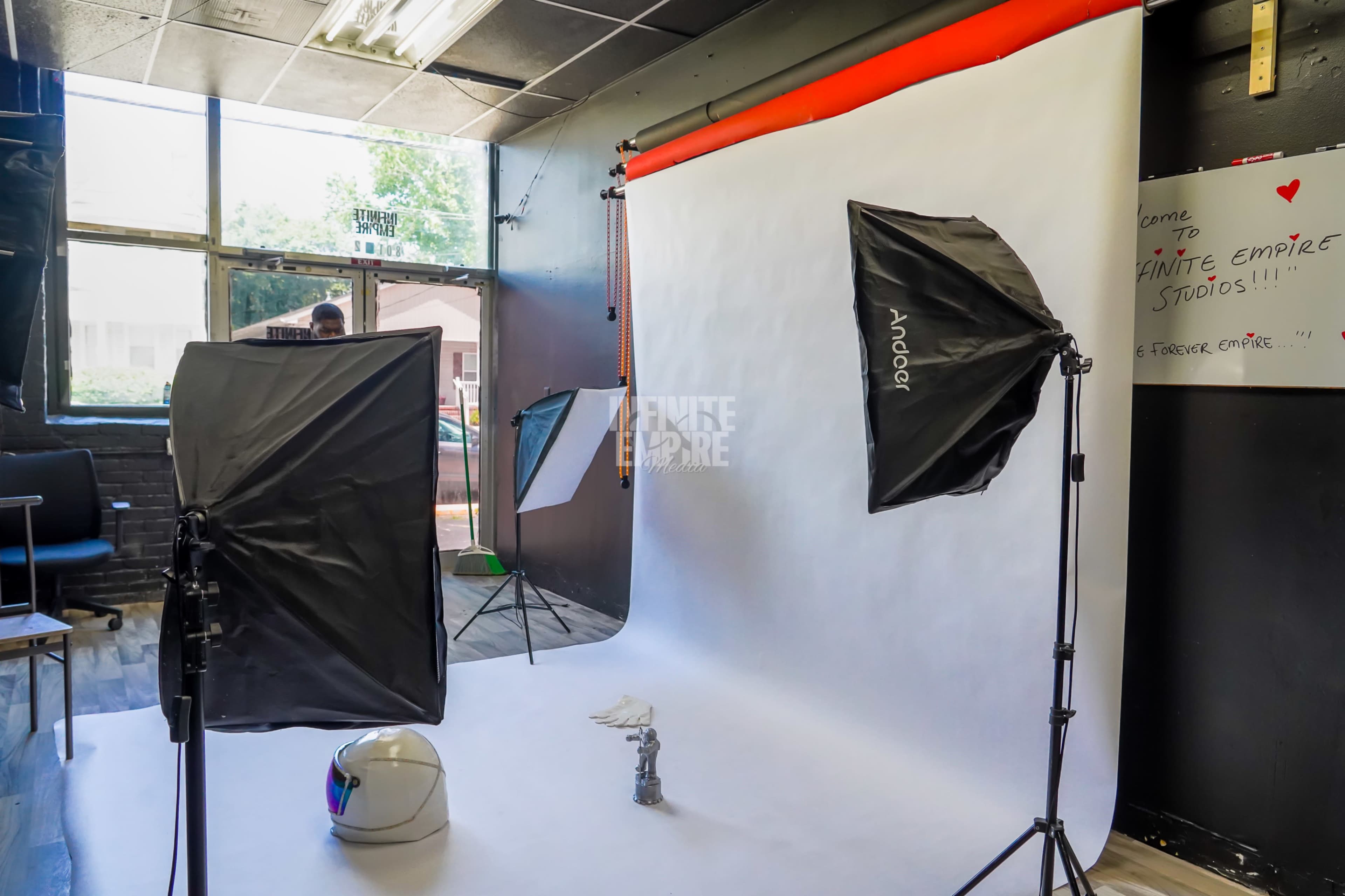 The image shows a photography studio setup with a white backdrop, softbox lights on either side, and a small object placed on the floor in front of the backdrop.