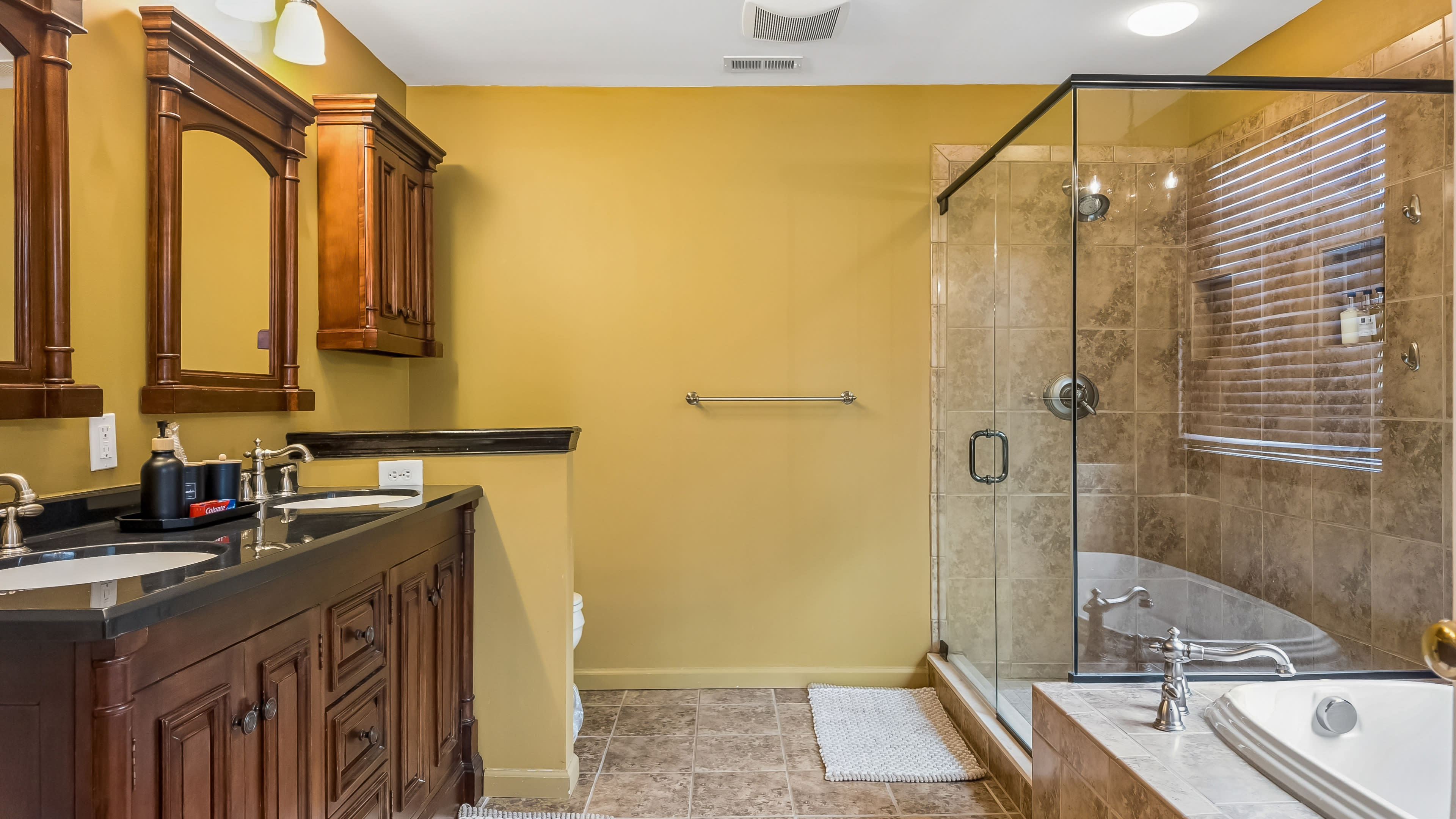 The image shows a bathroom featuring a glass shower, a bathtub, and wooden cabinetry with dual sinks.