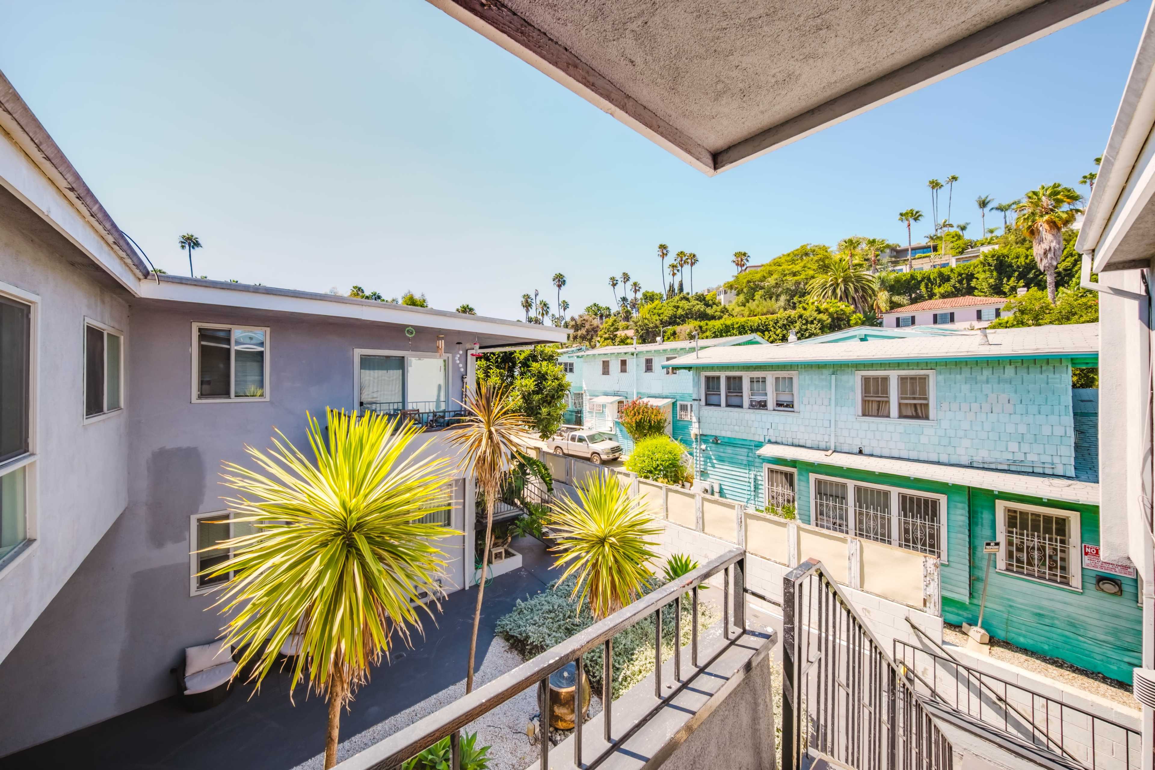 The image shows a view from a balcony overlooking an alley with palm trees and colorful buildings on either side.