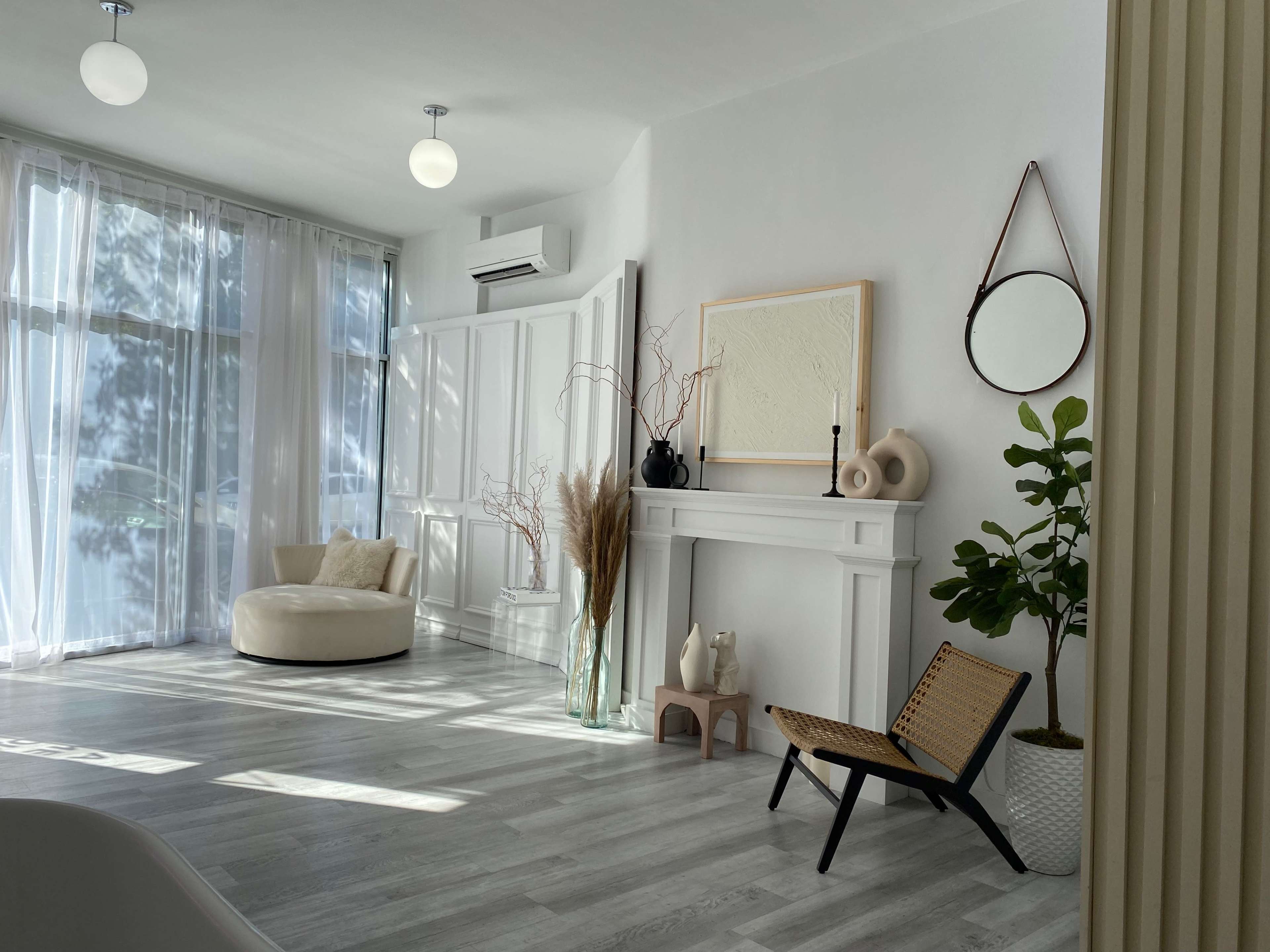 A bright, modern living room with white walls, a large window, a decorative fireplace, and minimalistic furniture.