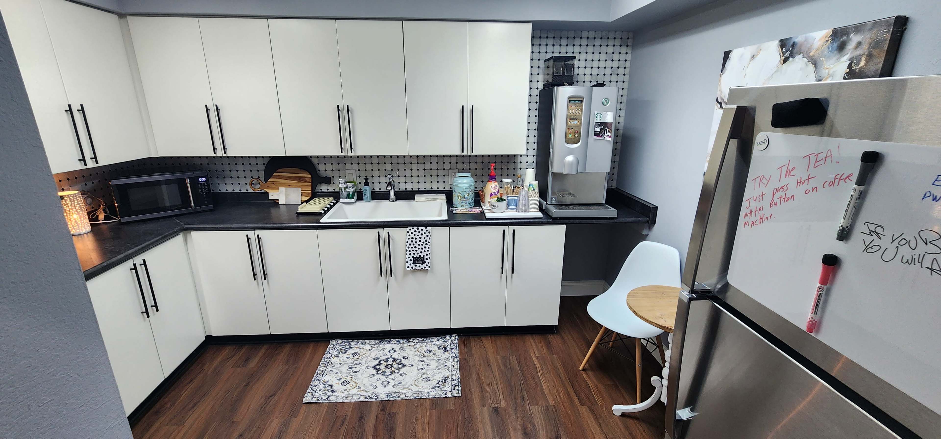 A compact kitchen with white cabinets, a dark countertop, a small dining table, and various kitchen appliances.