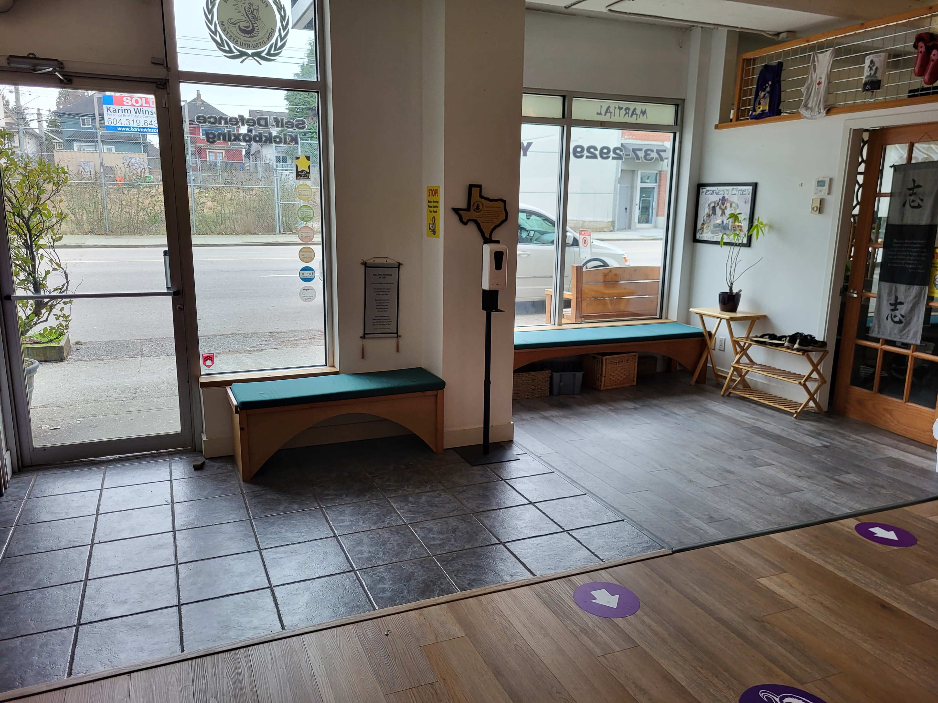 The image shows the interior of a business space featuring a tiled entrance area, benches along the walls, and a hand sanitizer station near the entrance.