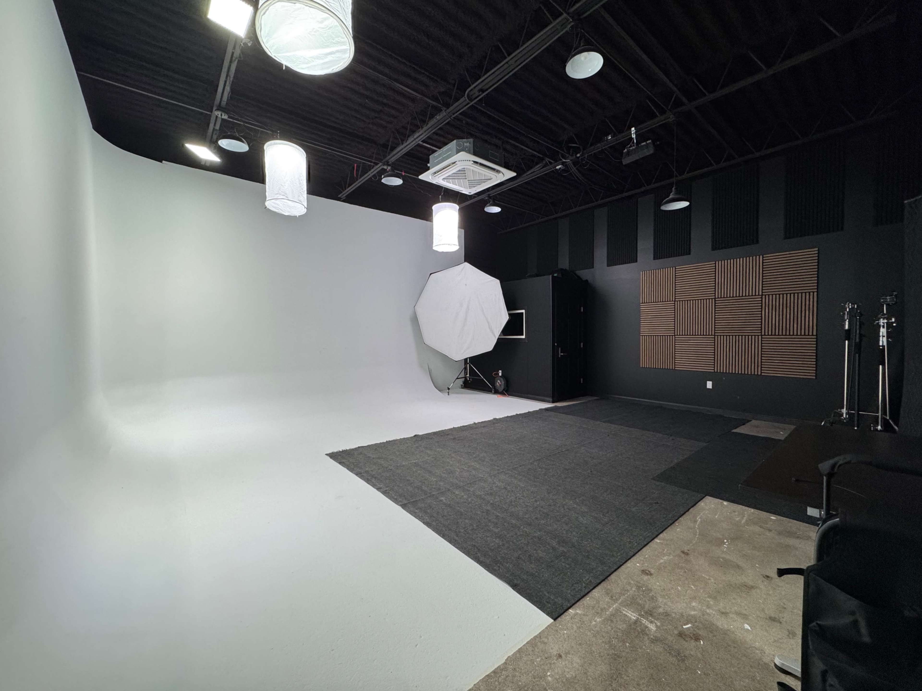 The image shows a photography studio with a white backdrop, lighting equipment, and a textured wooden wall panel.