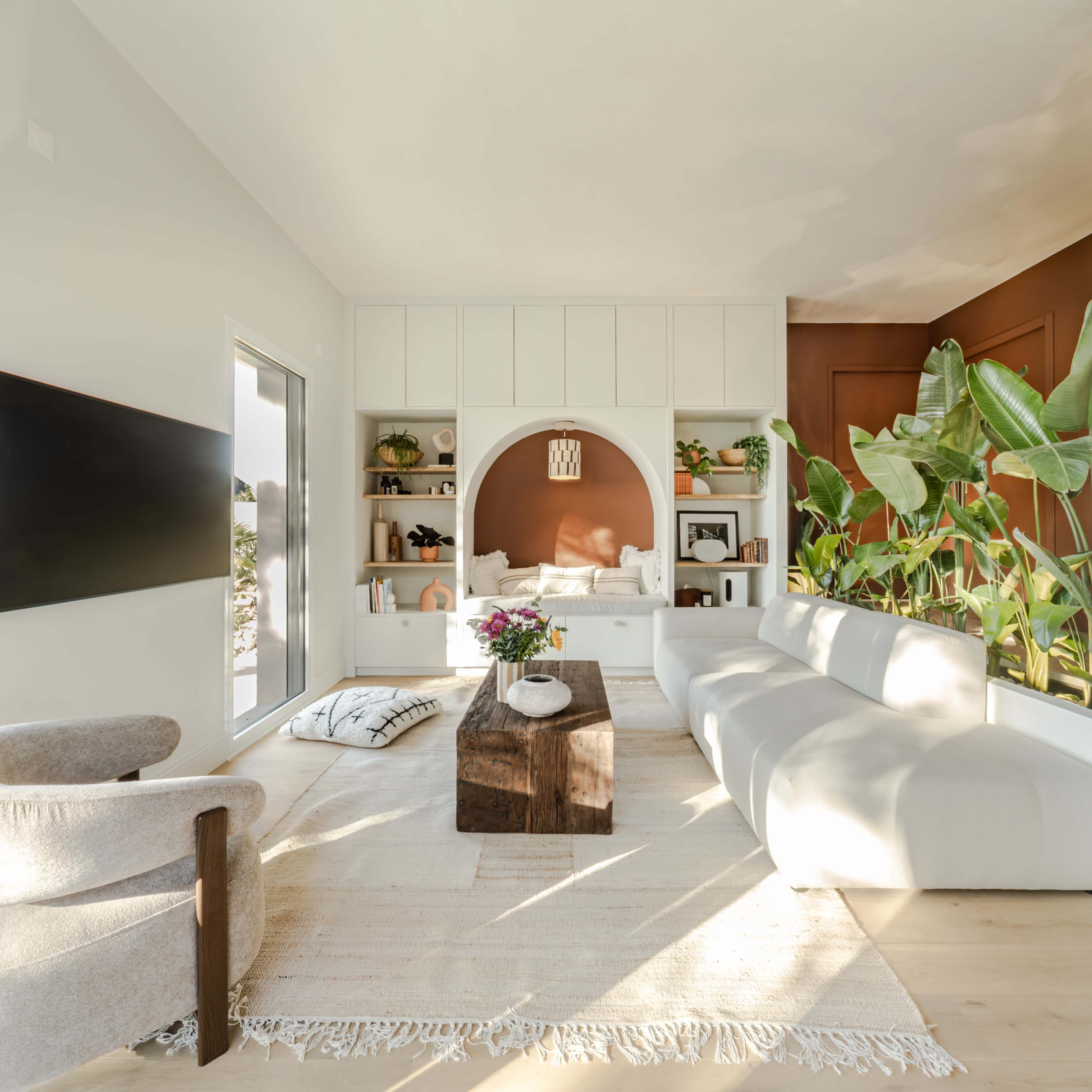 The living room features a light gray sofa, a wooden coffee table, and a built-in shelf with decorative items against a backdrop of warm brown paint.