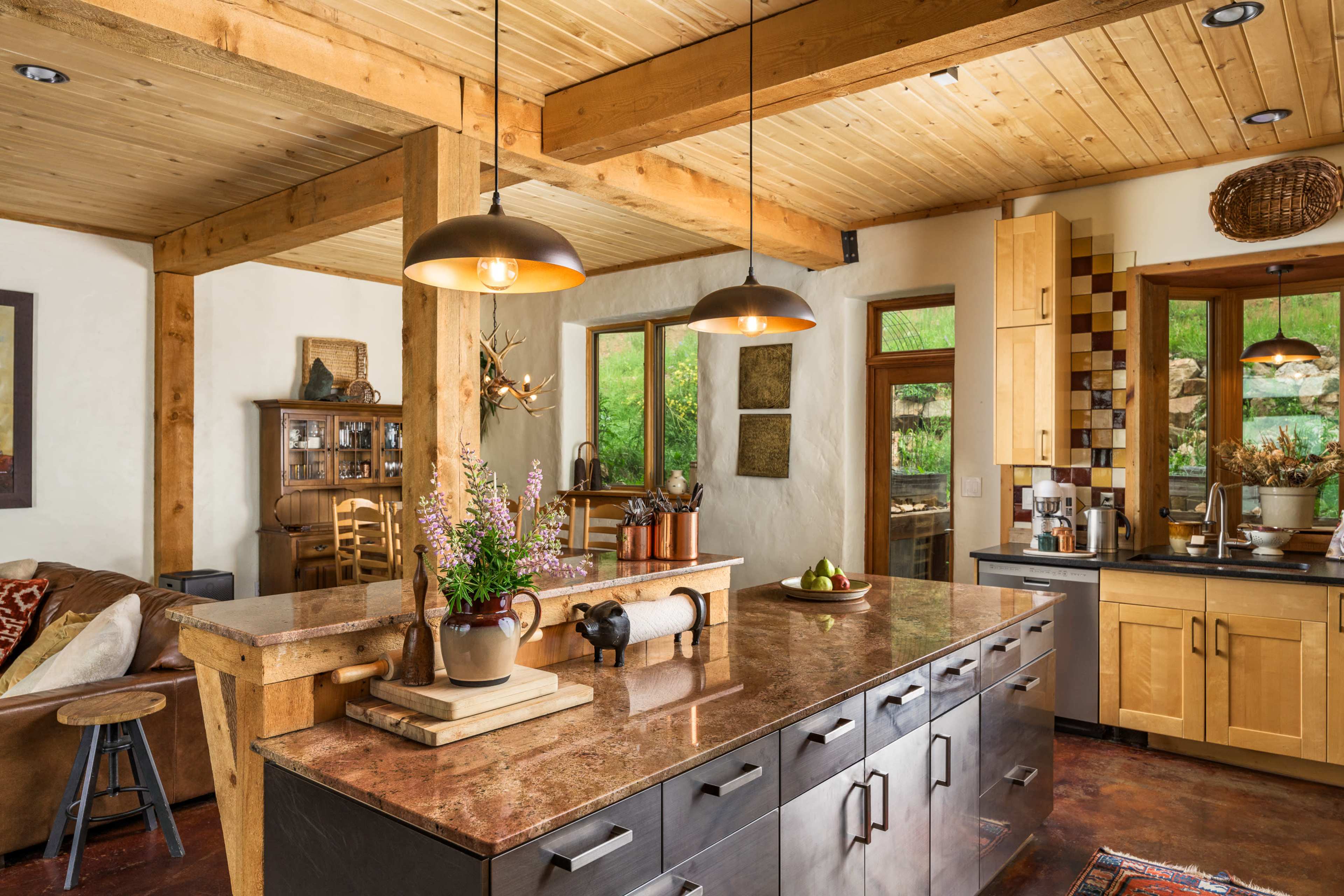 The kitchen features a central island with a stone countertop, surrounded by wooden beams and pendant lighting.