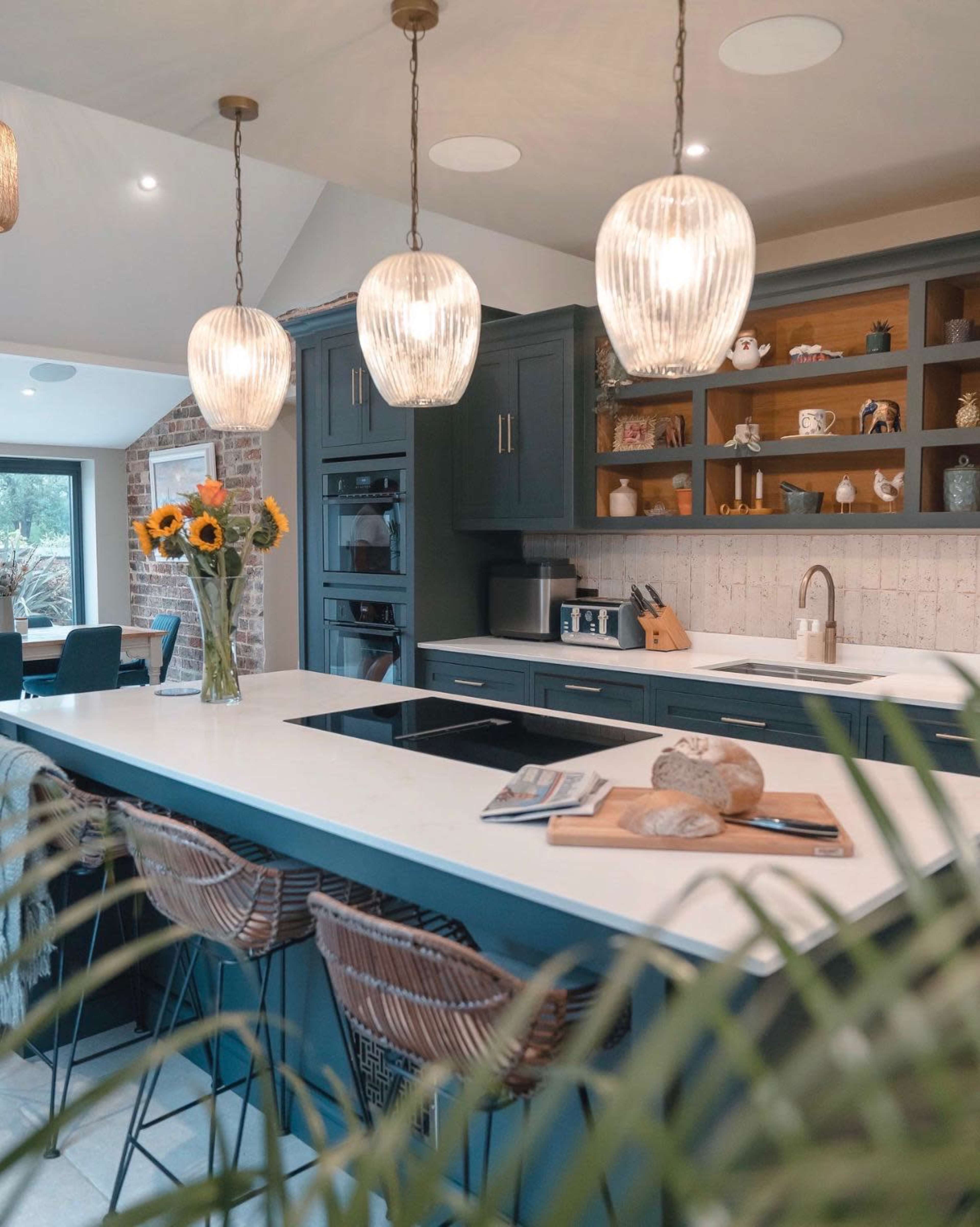 The image features a modern kitchen with blue cabinets, pendant lighting, a central island, and a vase of sunflowers on the countertop.