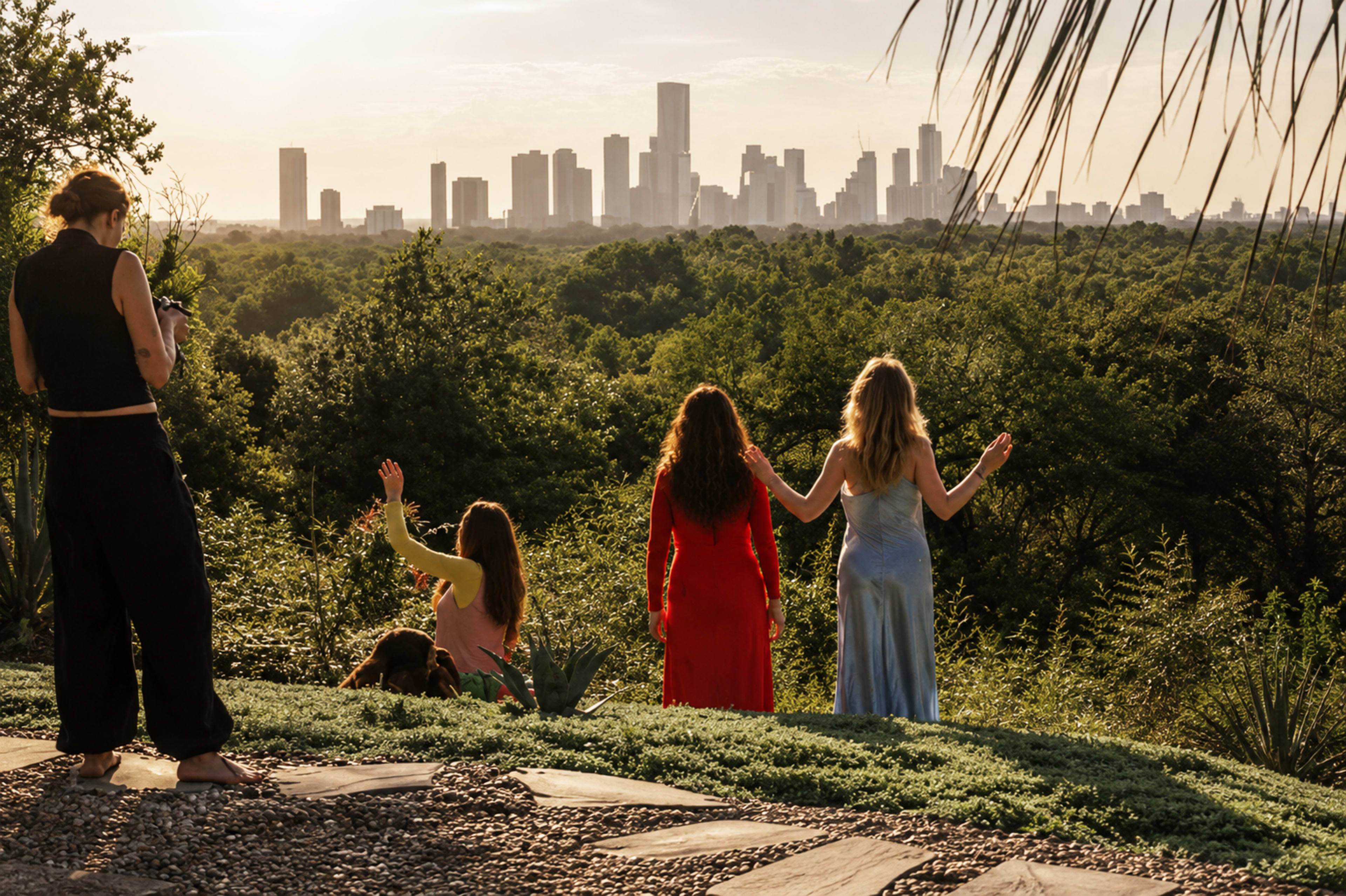 A group of women stands on a hillside overlooking a city skyline during sunset.