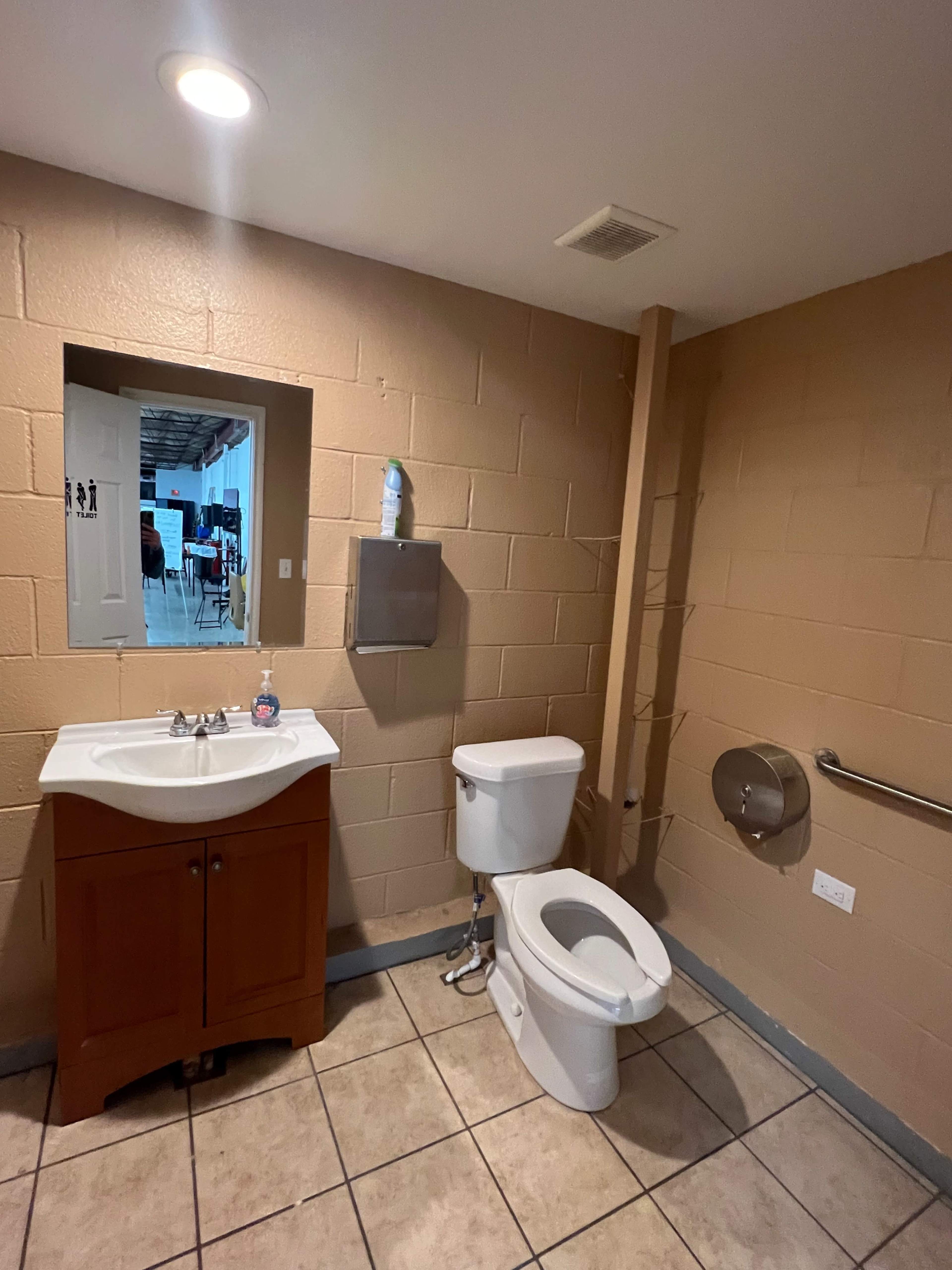 A bathroom with a toilet, a sink with a cabinet, and a mirror against a beige wall.