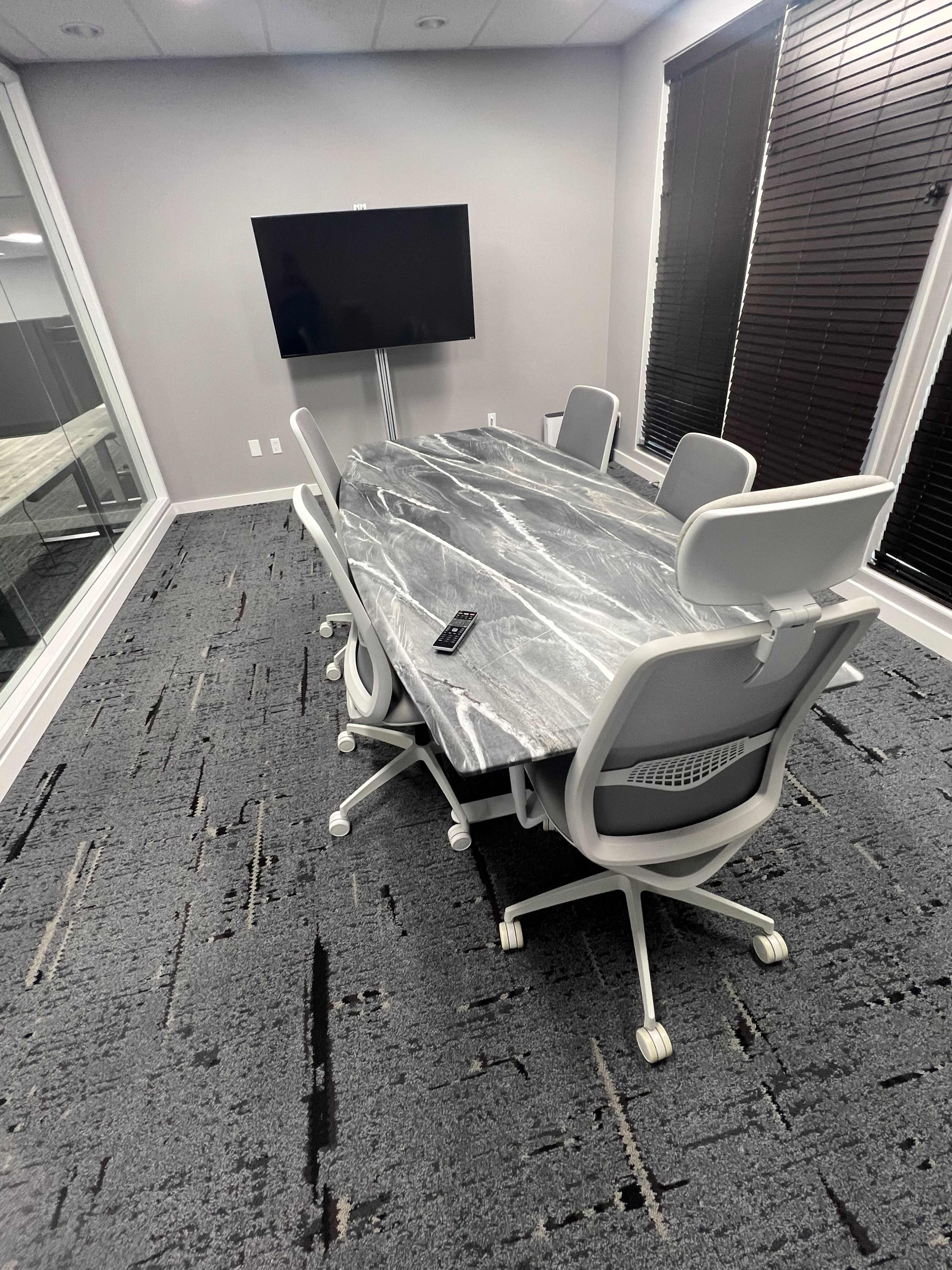 A modern conference room features a marble table surrounded by four ergonomic chairs and a wall-mounted television.