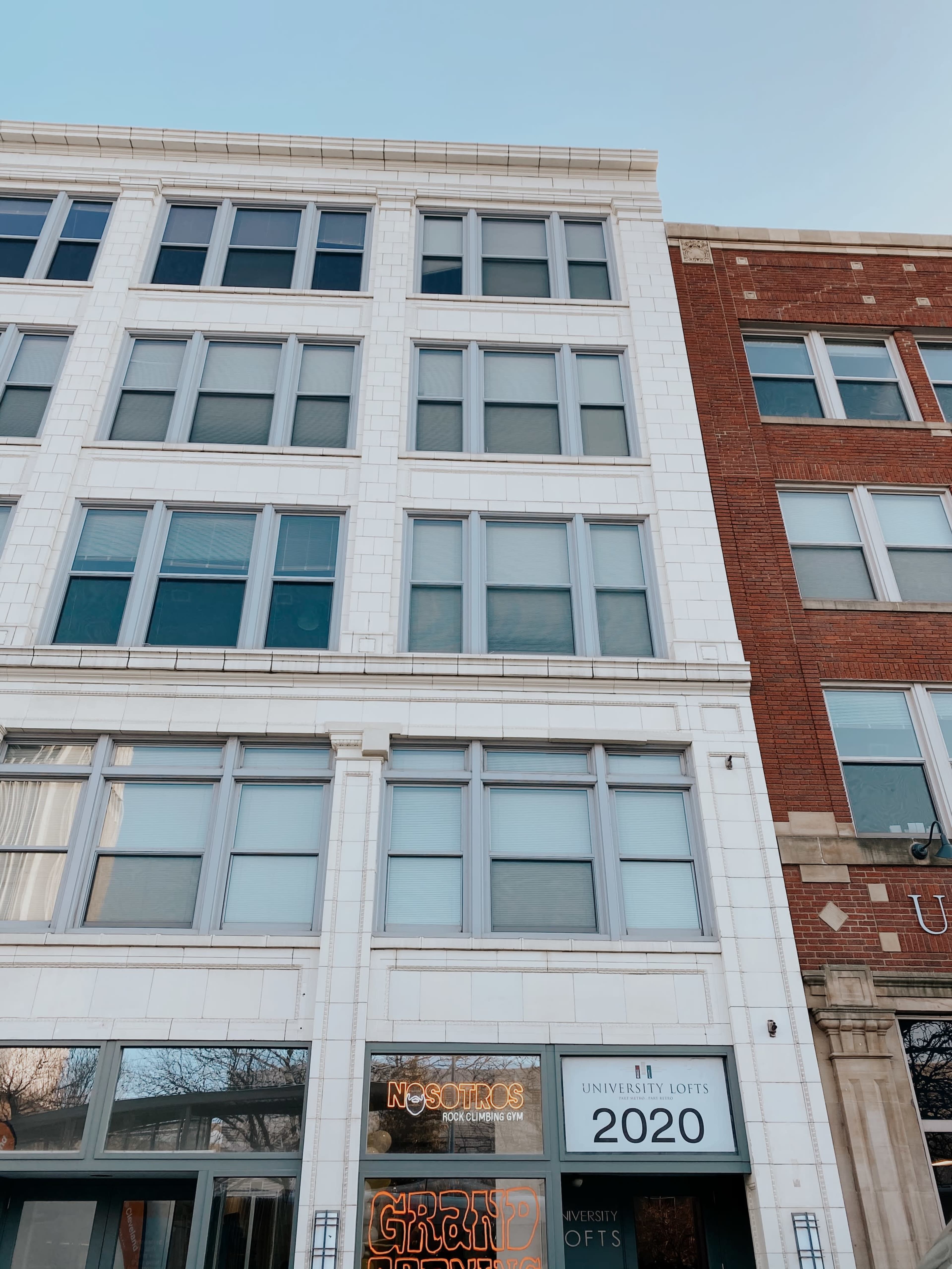 A multi-story building facade featuring large windows and a sign for "University Lofts" along with another sign for "Nosotros."