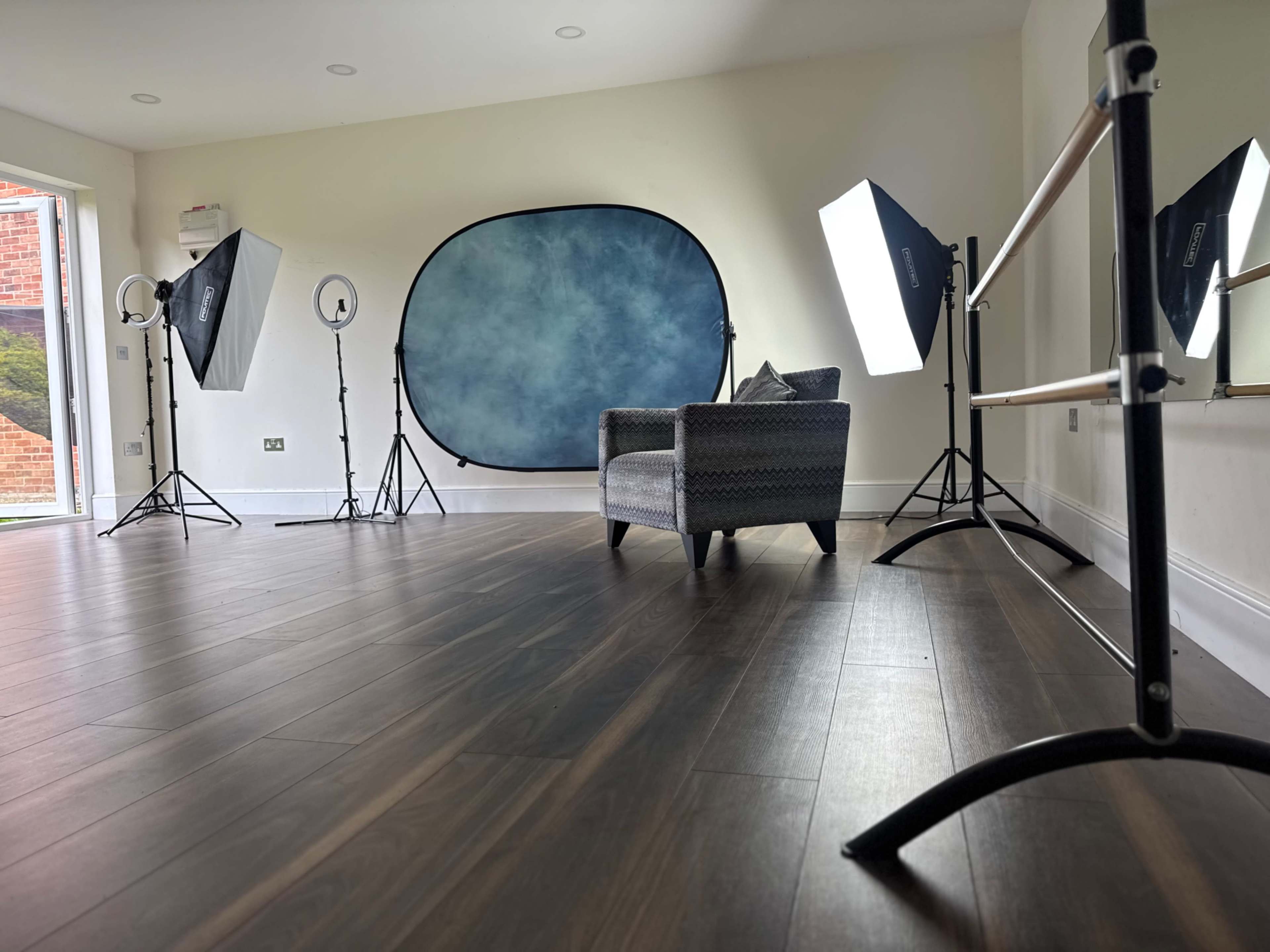 The image shows a well-lit studio space featuring a patterned chair, a blue backdrop, and several professional lighting equipment setups.