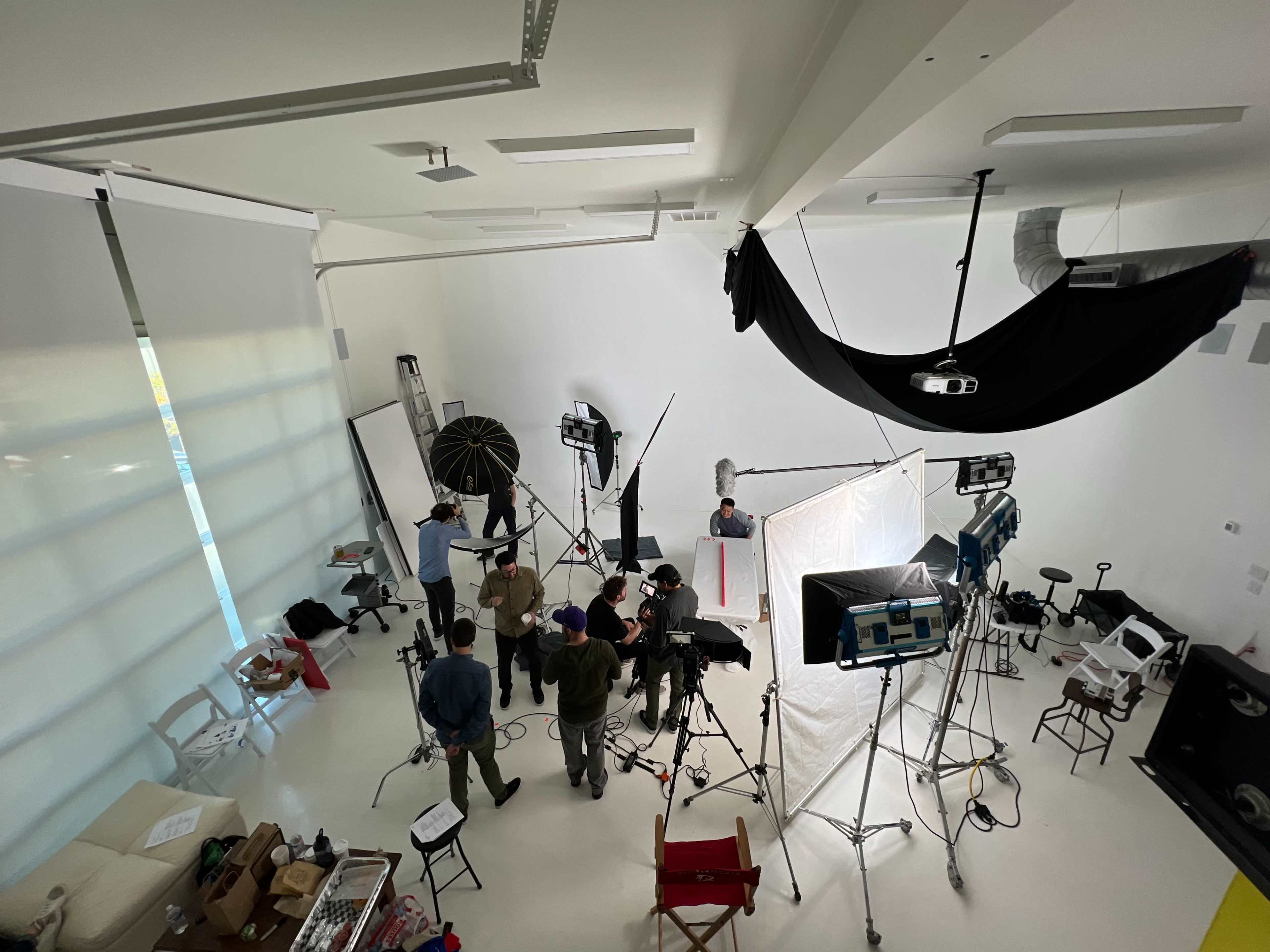 A film crew sets up equipment in a bright studio for a production shoot.