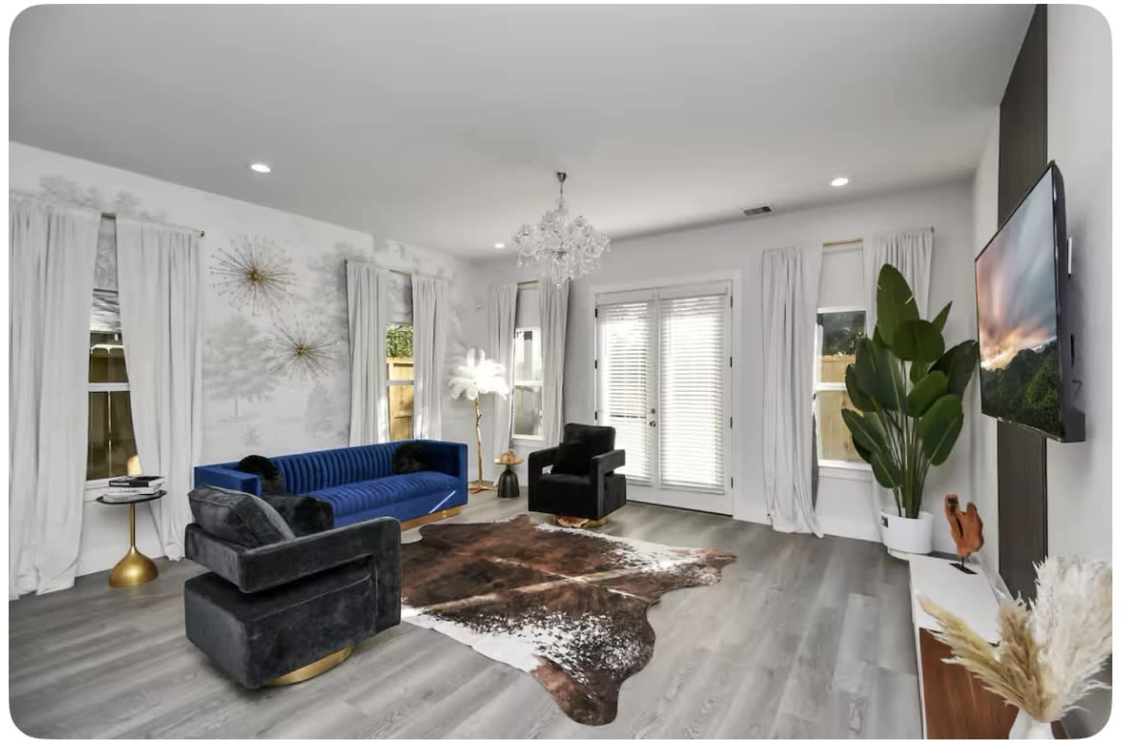 The living room features a blue sofa, black armchairs, a cowhide rug, and large windows with sheer white curtains.