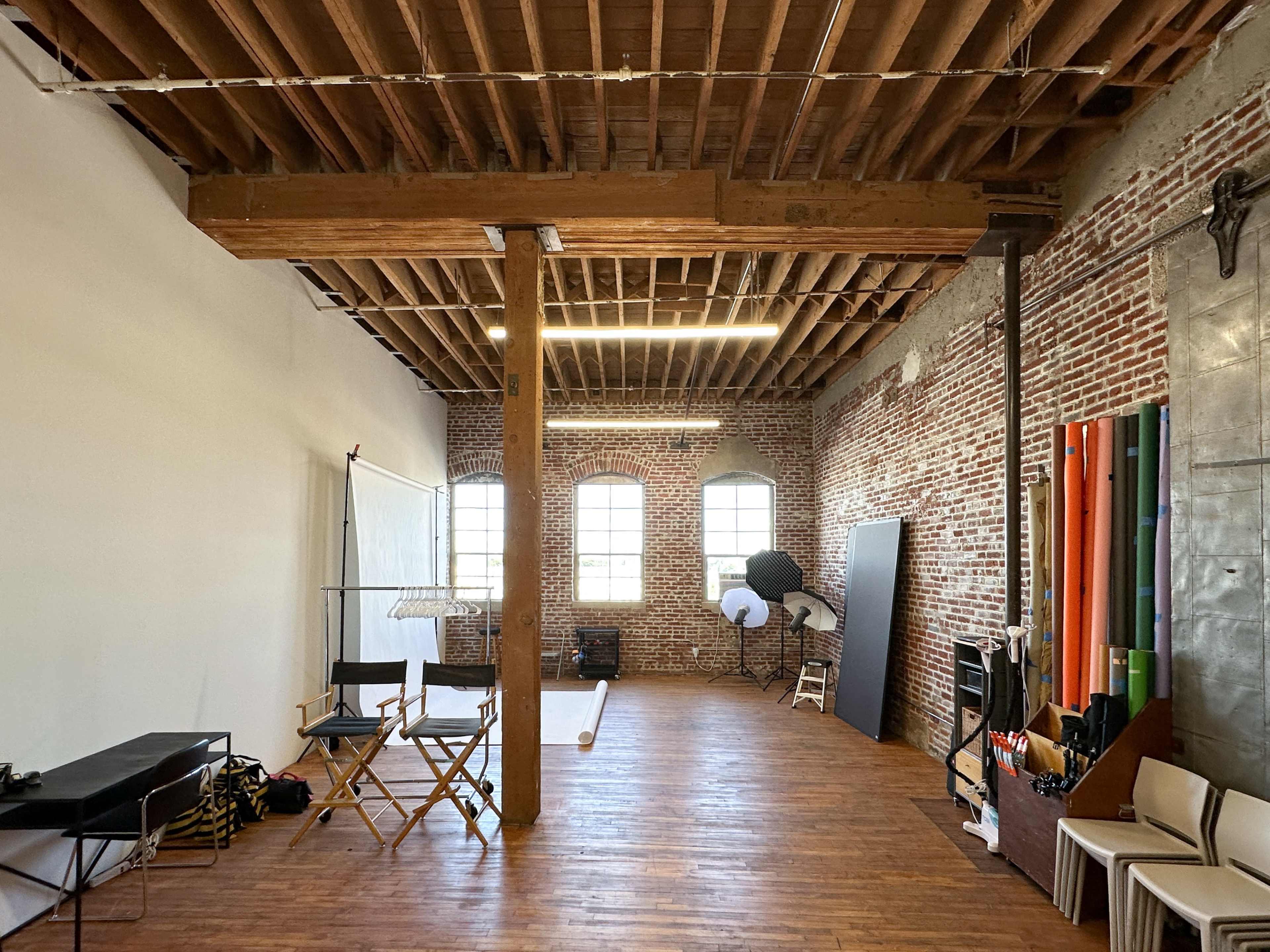 The image shows an expansive photography studio with exposed brick walls, wooden beams, and various equipment set up for shoots.