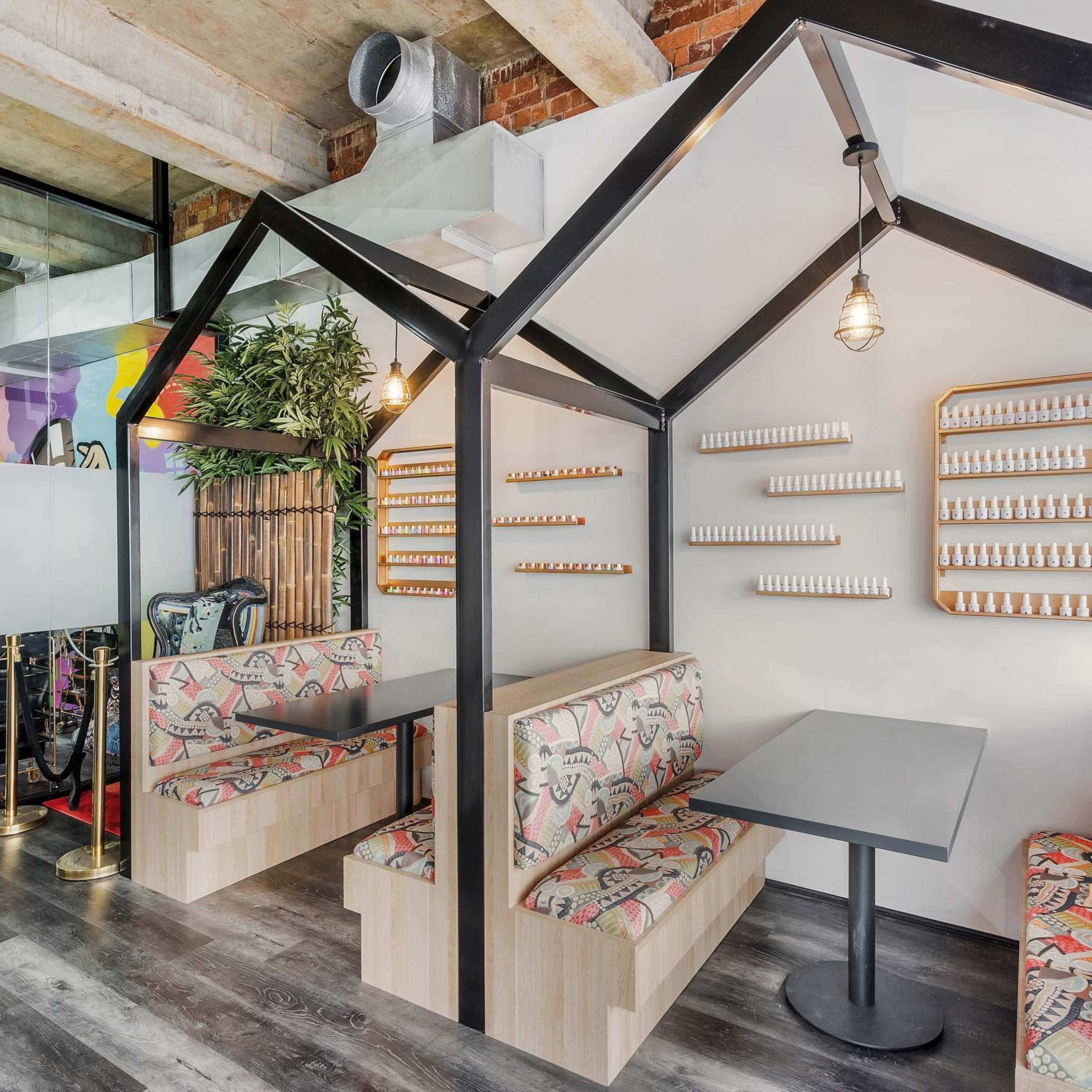A modern café interior featuring two cozy seating areas with patterned upholstery, surrounded by wood and metal elements.