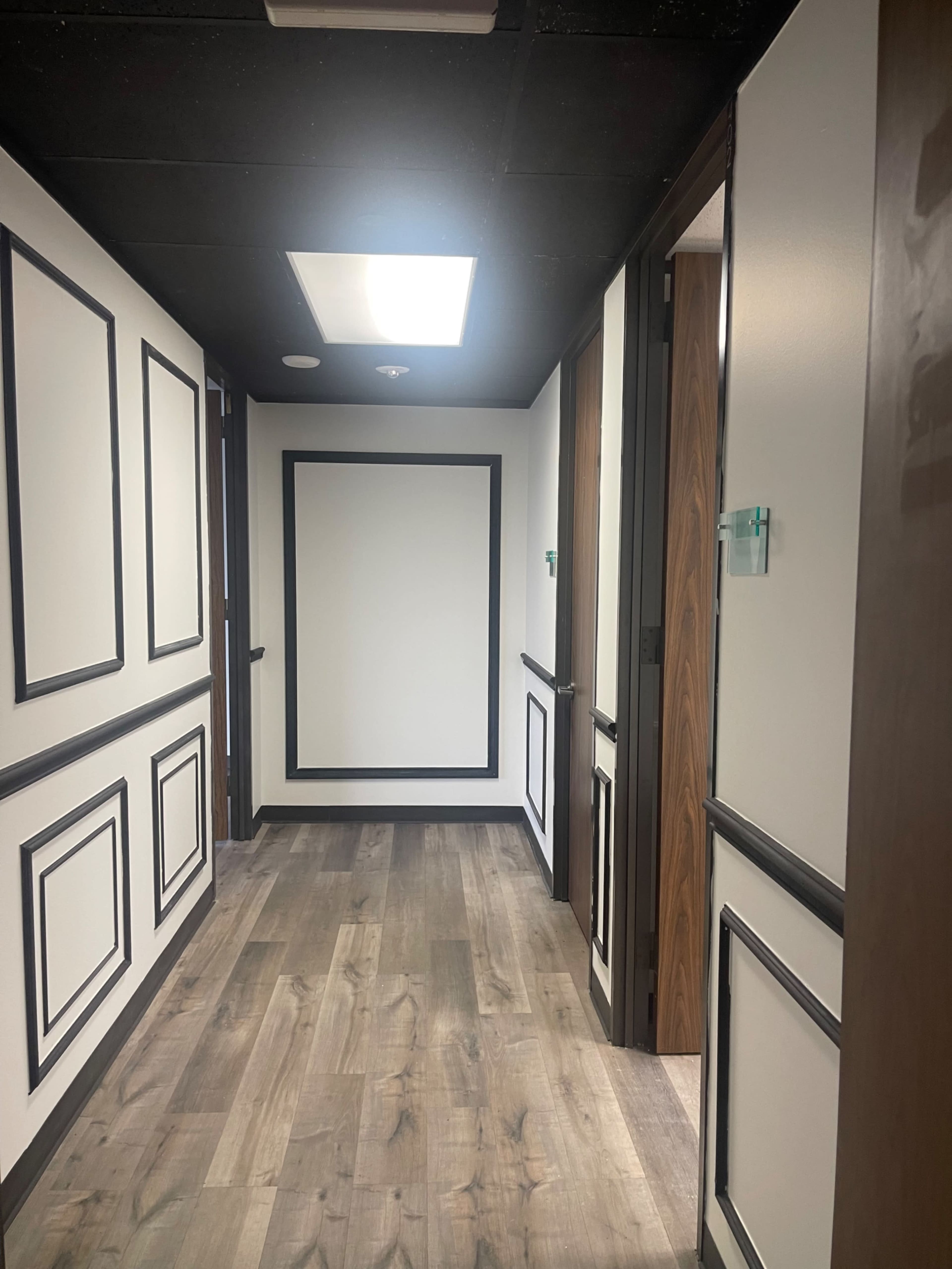 The image shows a corridor with black and white wall paneling, wooden flooring, and doors on either side.