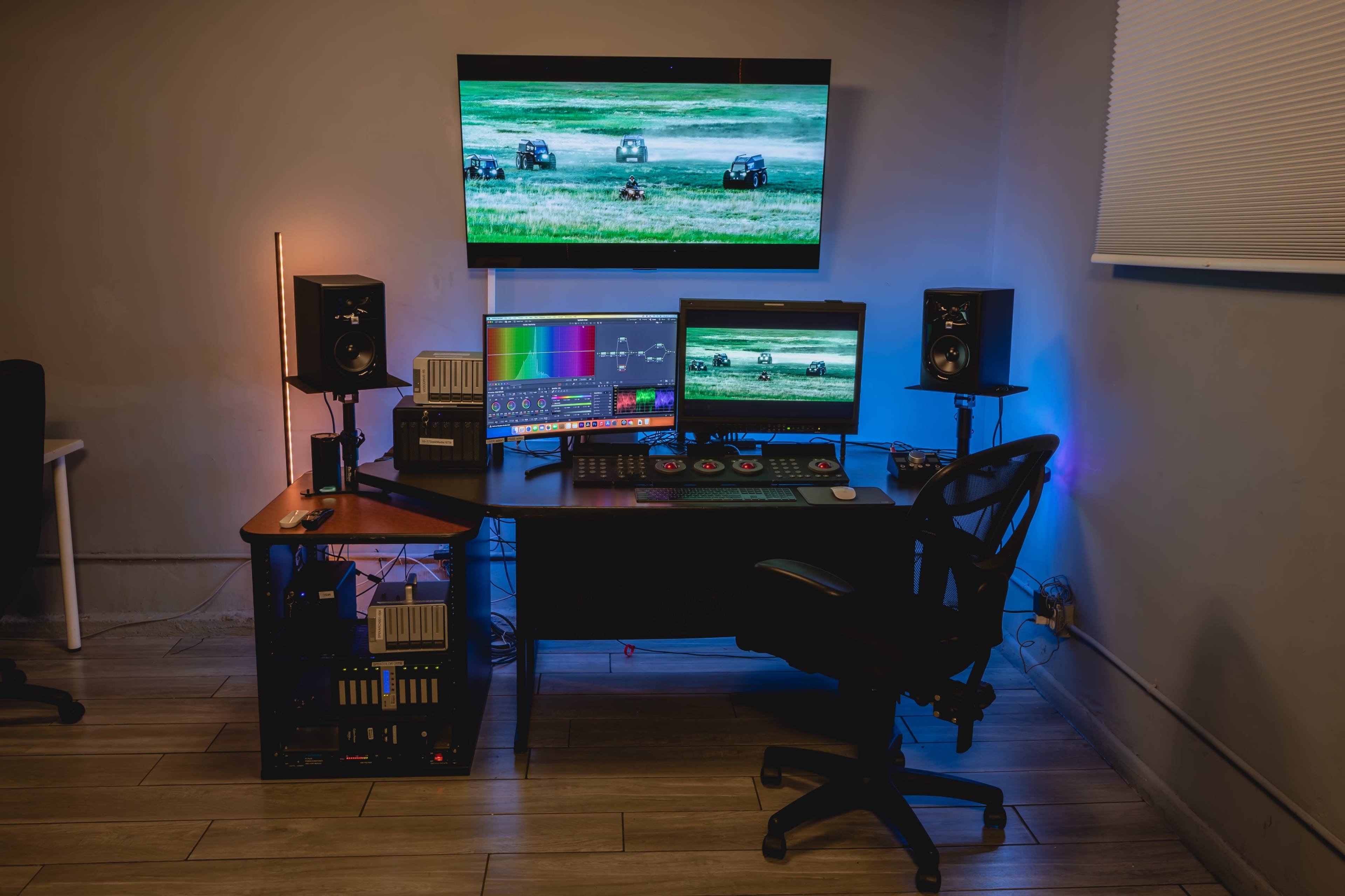 A modern computer workstation features multiple monitors, speakers, and colorful lighting, set against a neutral wall.