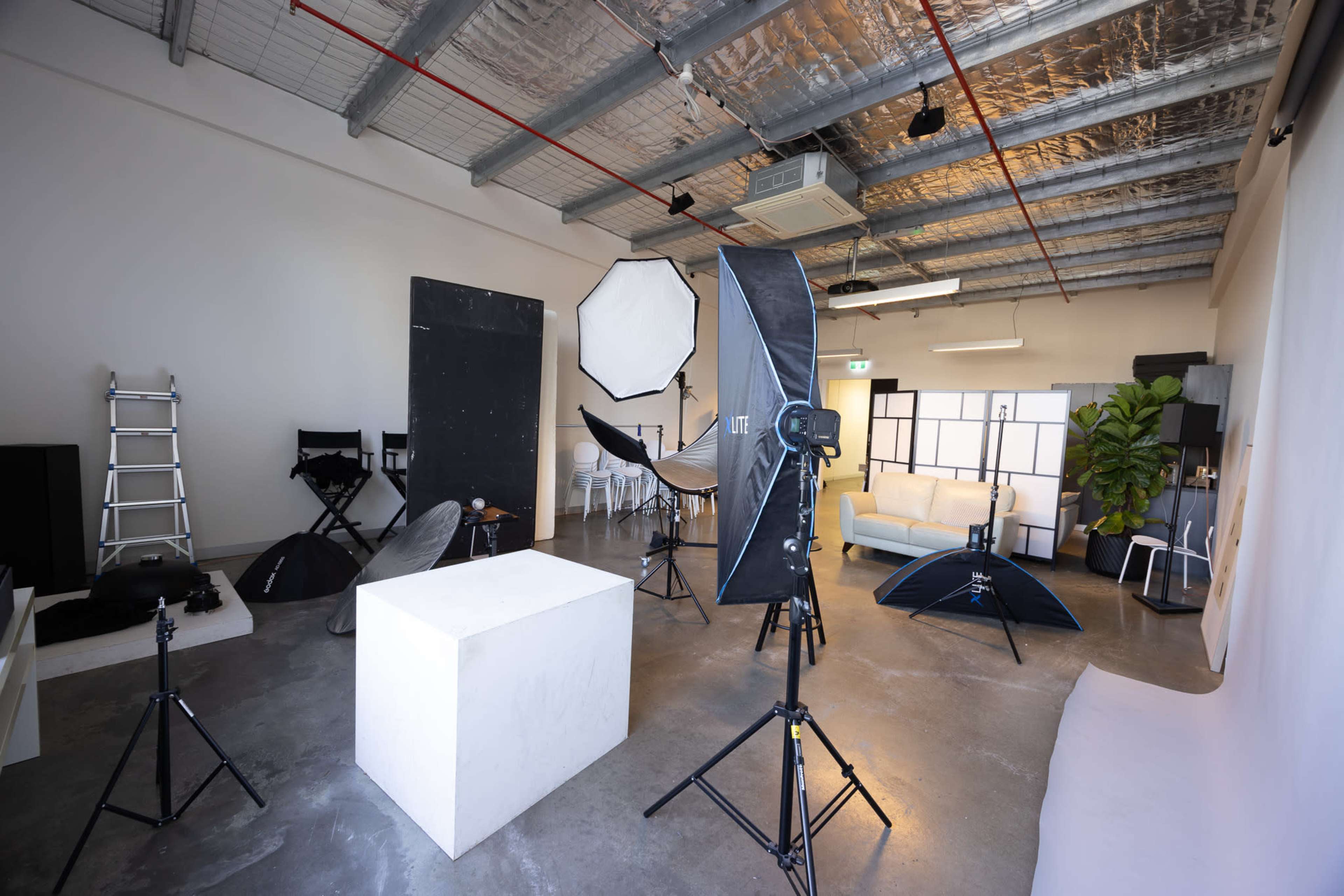 The image shows a photography studio with various lighting equipment, backdrops, and seating arrangements.