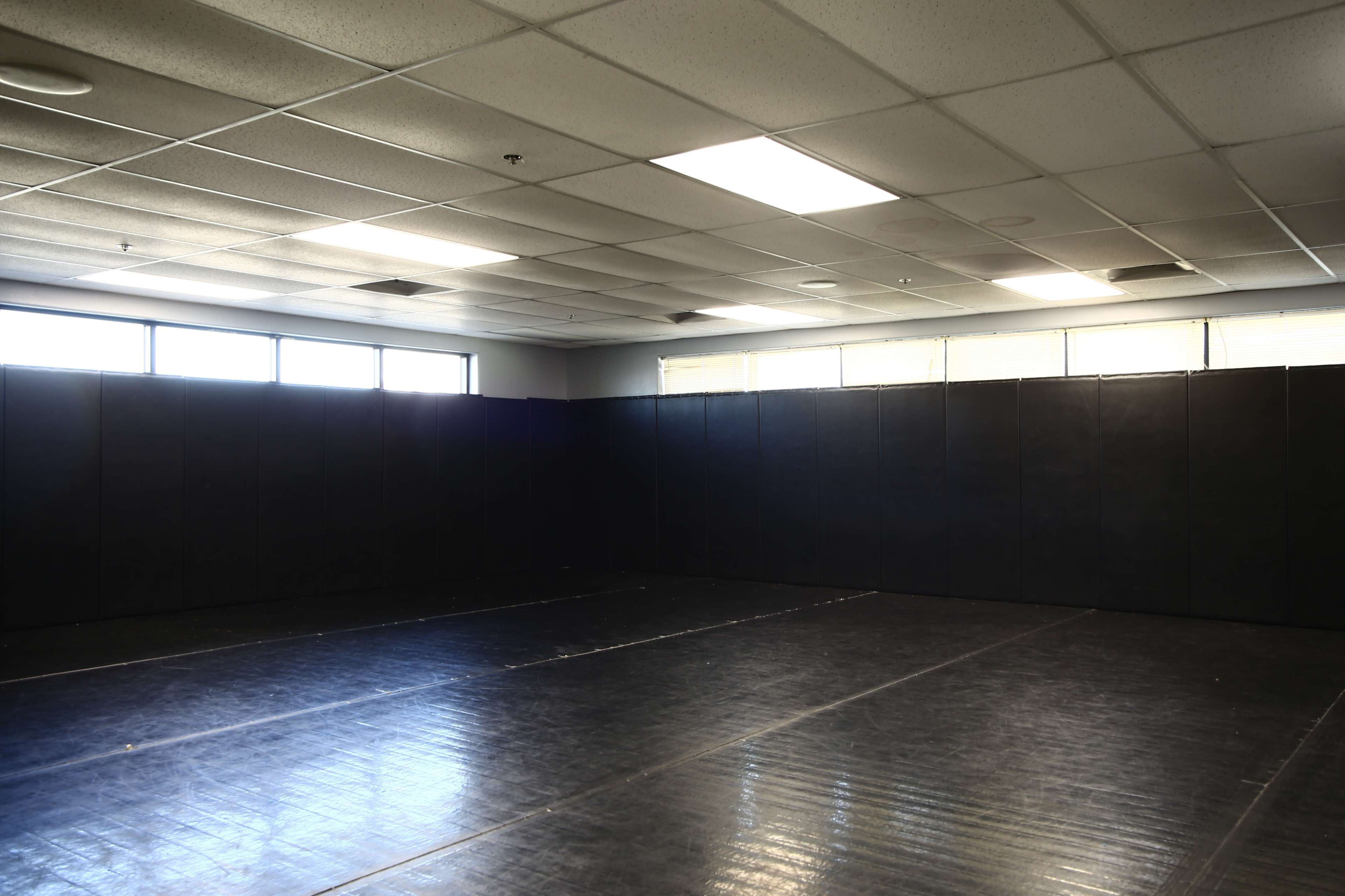 An unobstructed indoor space with black mats and padded walls, illuminated by overhead lighting.