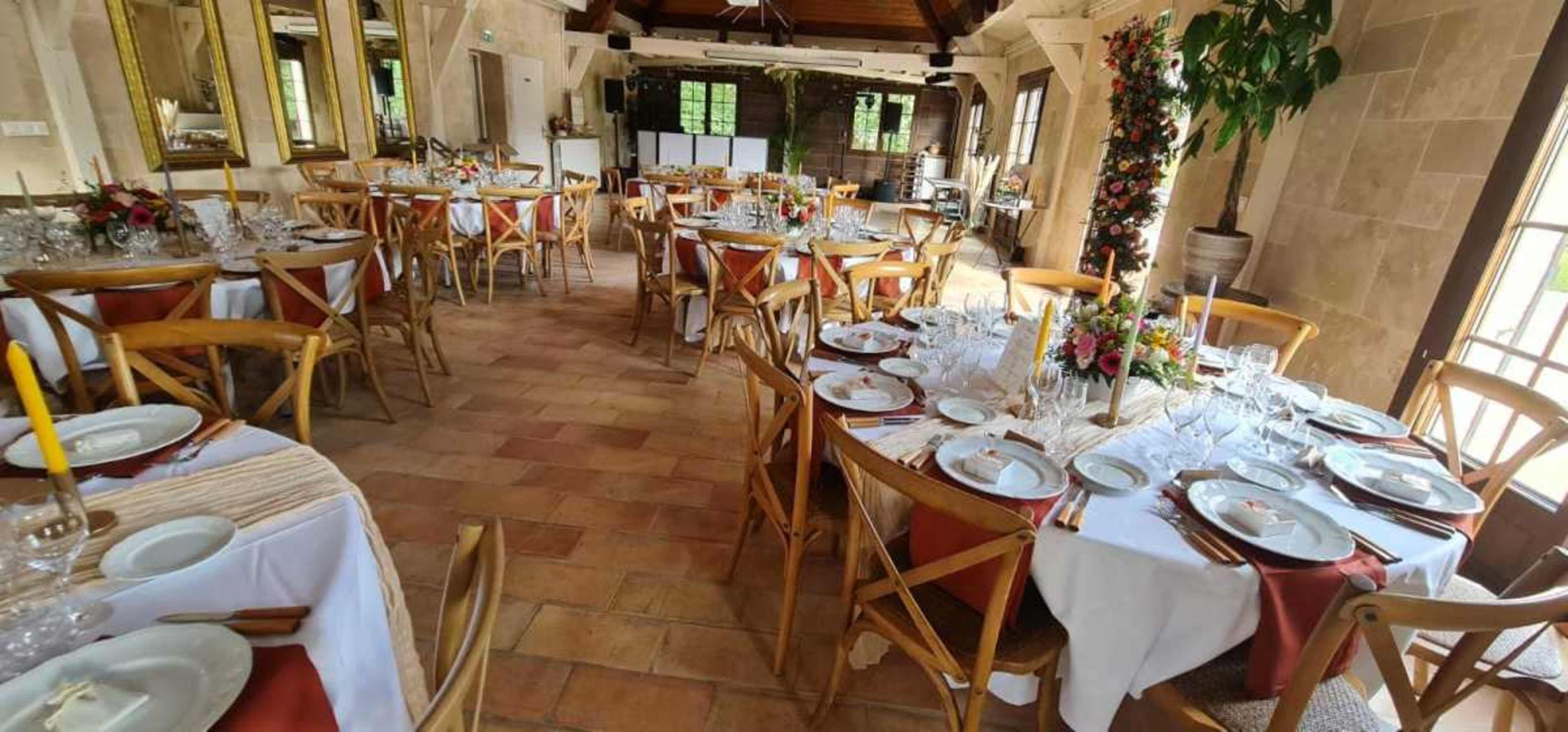 The image shows a dining area set up with multiple tables, each covered with white tablecloths and adorned with plates, glasses, and floral centerpieces.