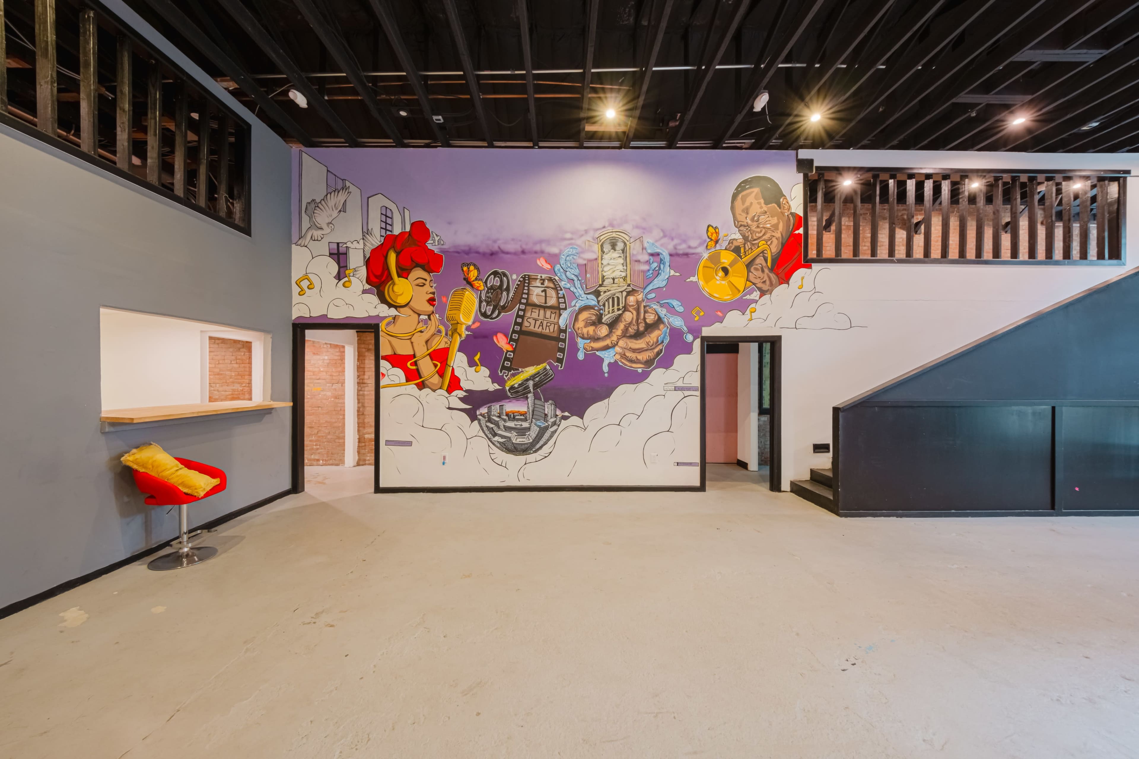 An open interior space featuring a vibrant mural on an accent wall, with a staircase in the corner and a small bar area visible.