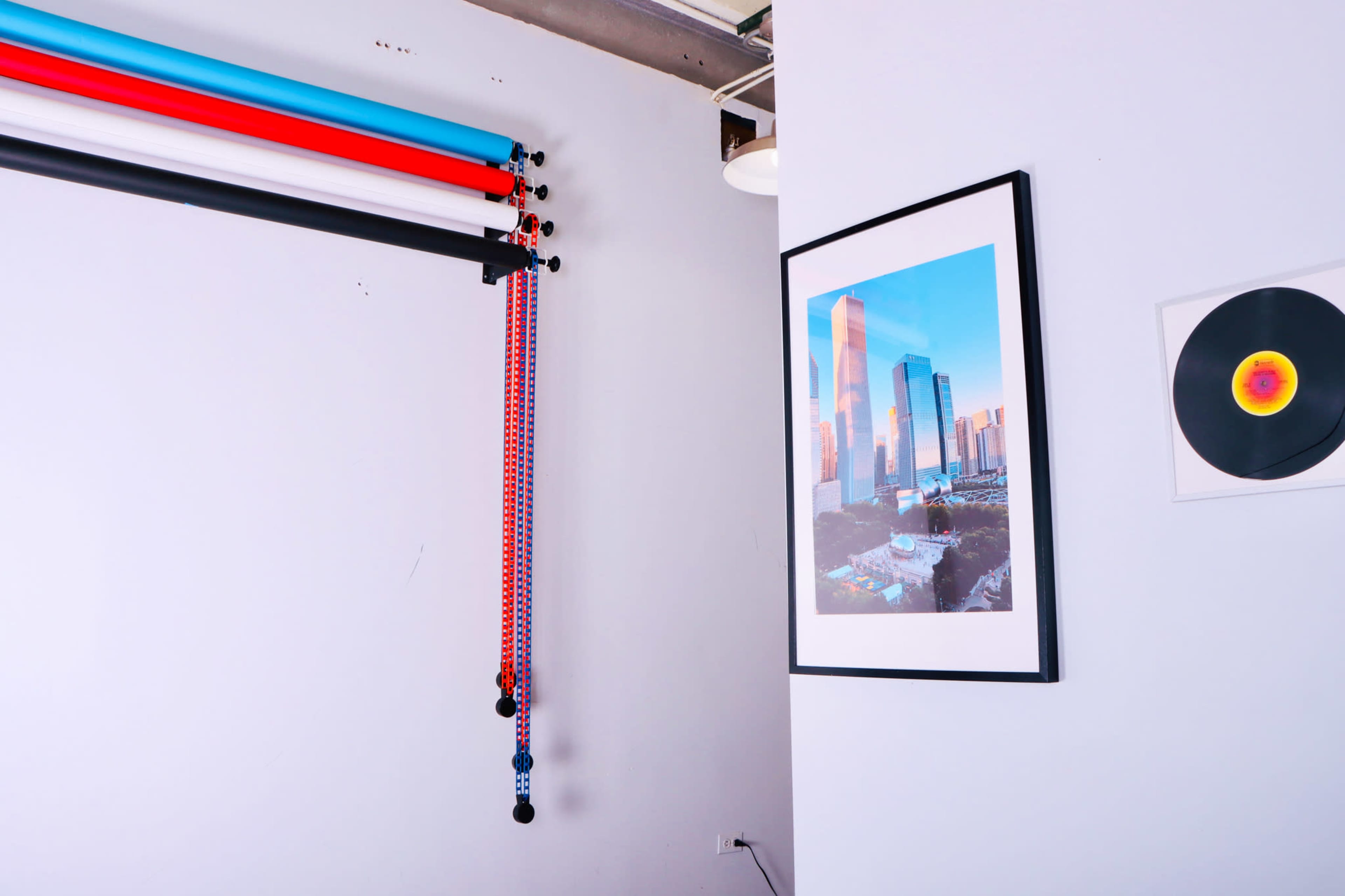 A corner of a room featuring colorful backdrop rolls mounted on the wall, two framed pictures, and a vinyl record on display.