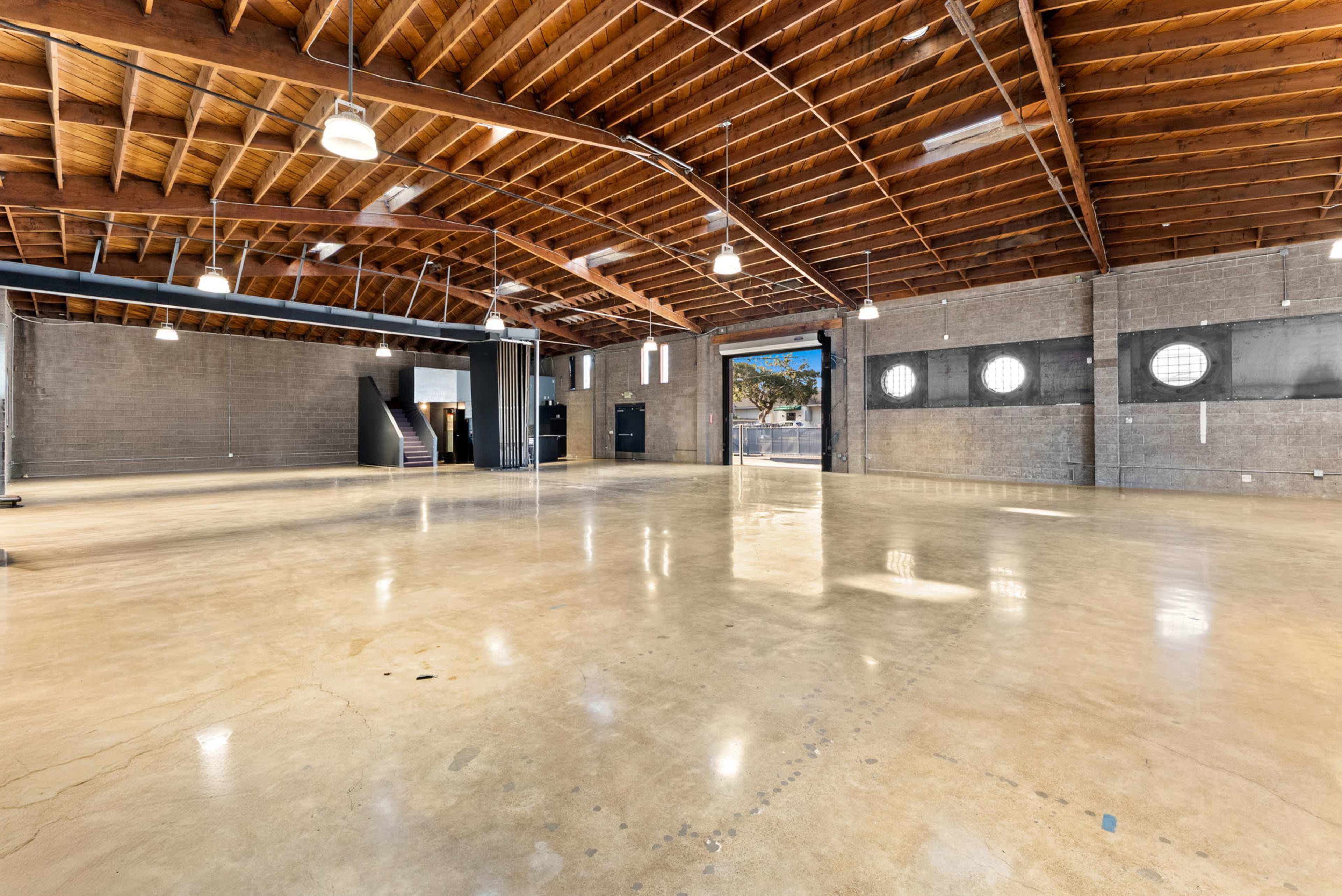 The image shows a spacious, open interior with polished concrete floors, wooden beams, and large windows, providing natural light.