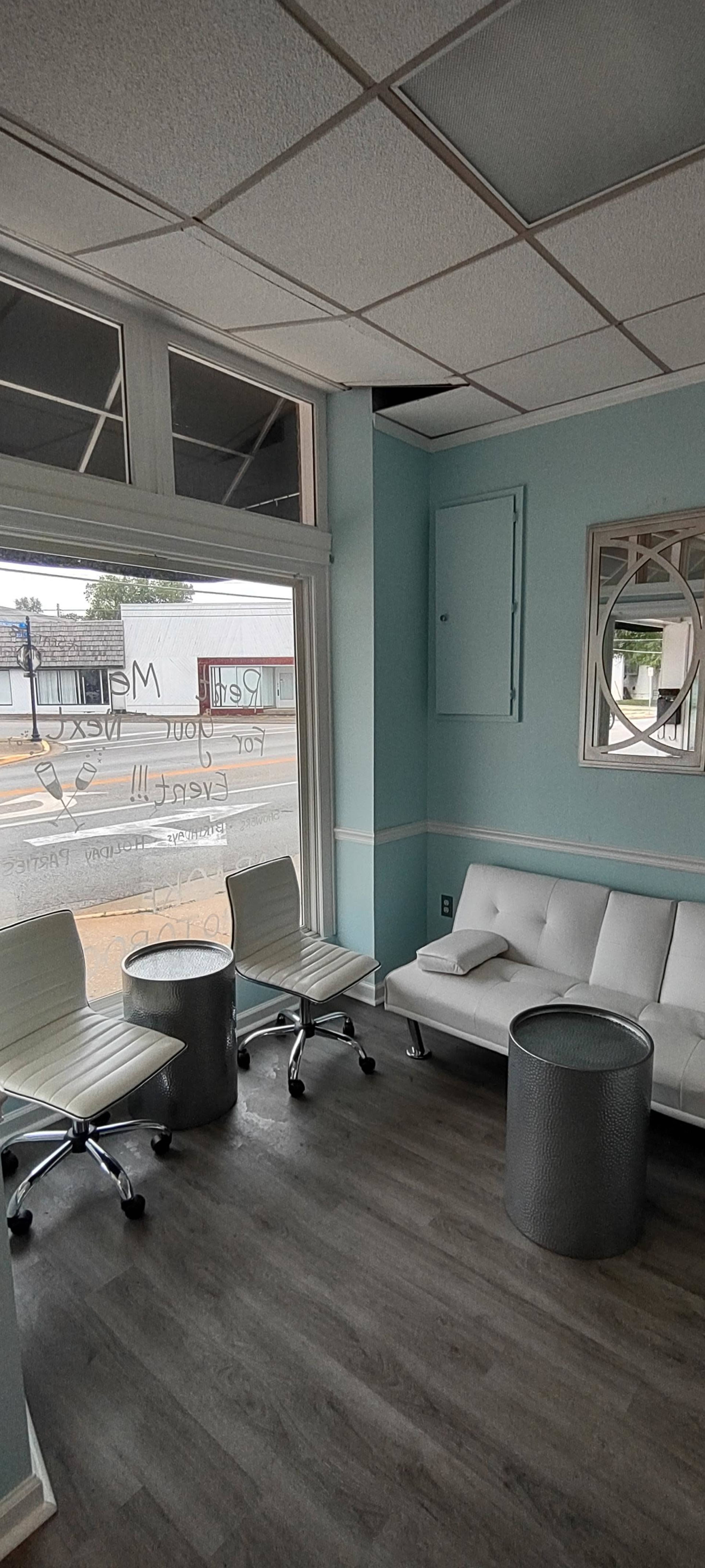 The image shows a waiting area with a white sofa, two modern chairs, and a round table, all set against a light blue wall.