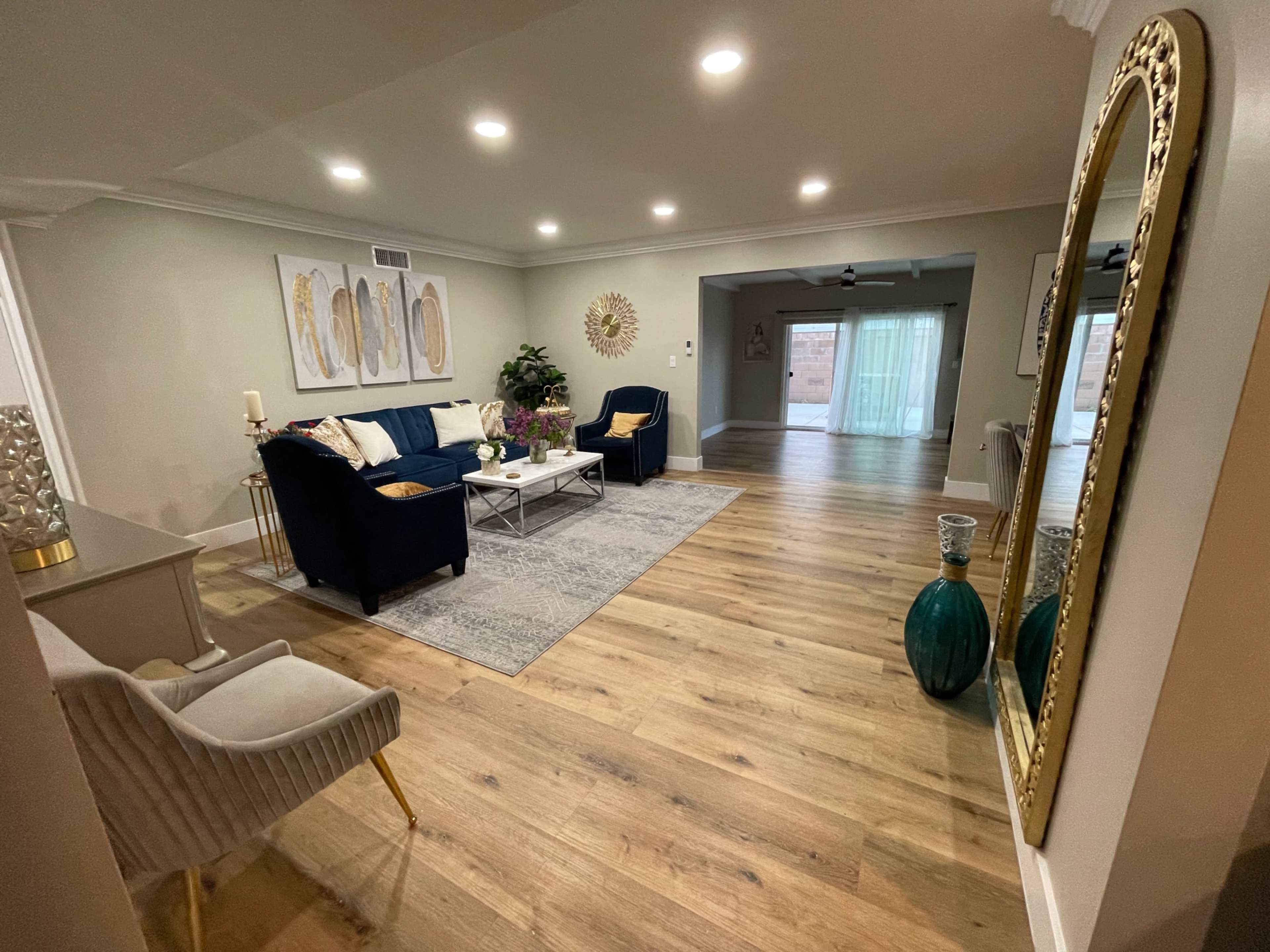A modern living room with navy blue couches, a coffee table, and light wood flooring, leading to an open area with sliding doors.