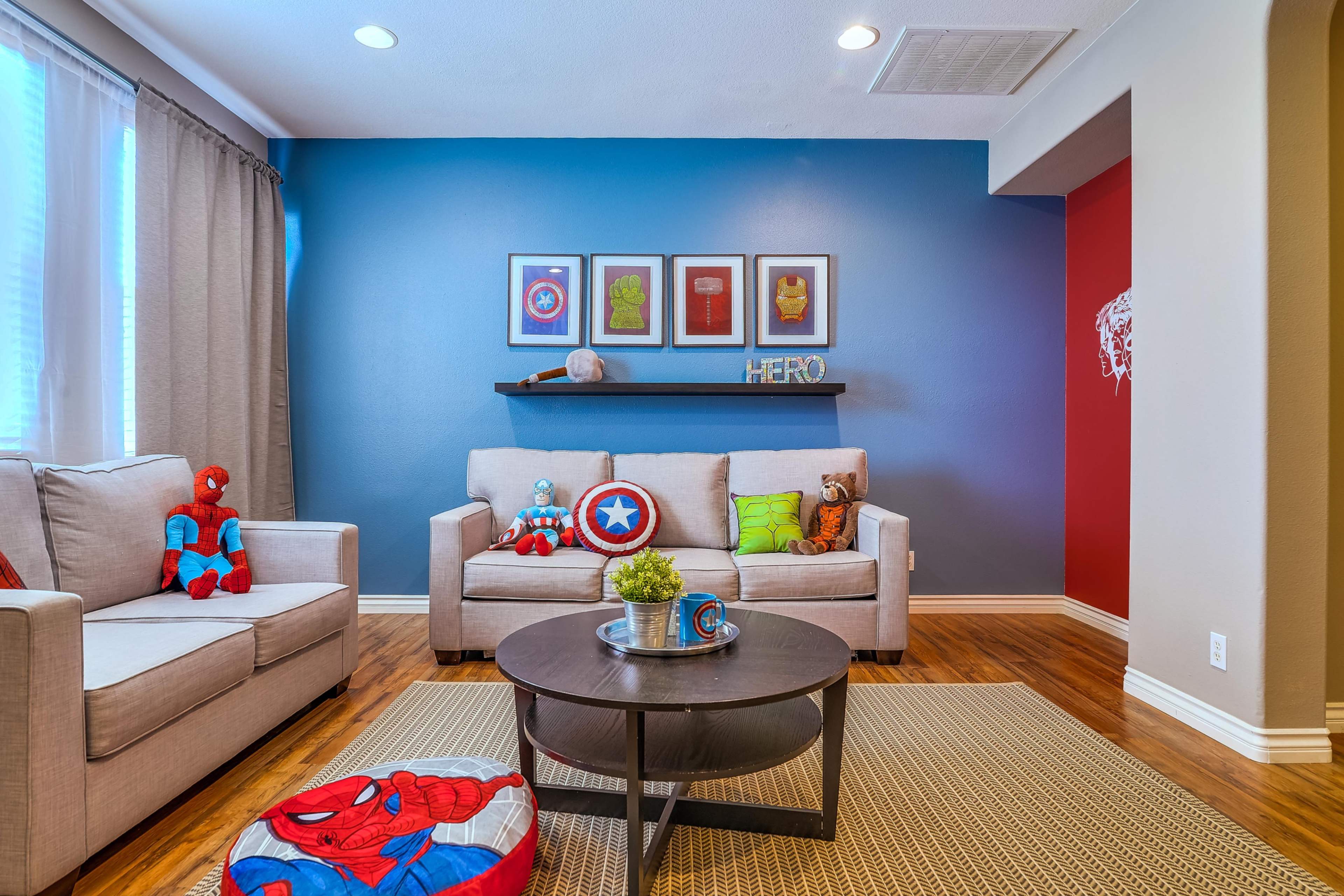 The living room features a gray sofa adorned with colorful cushions, a round coffee table, and a blue accent wall with framed artwork.