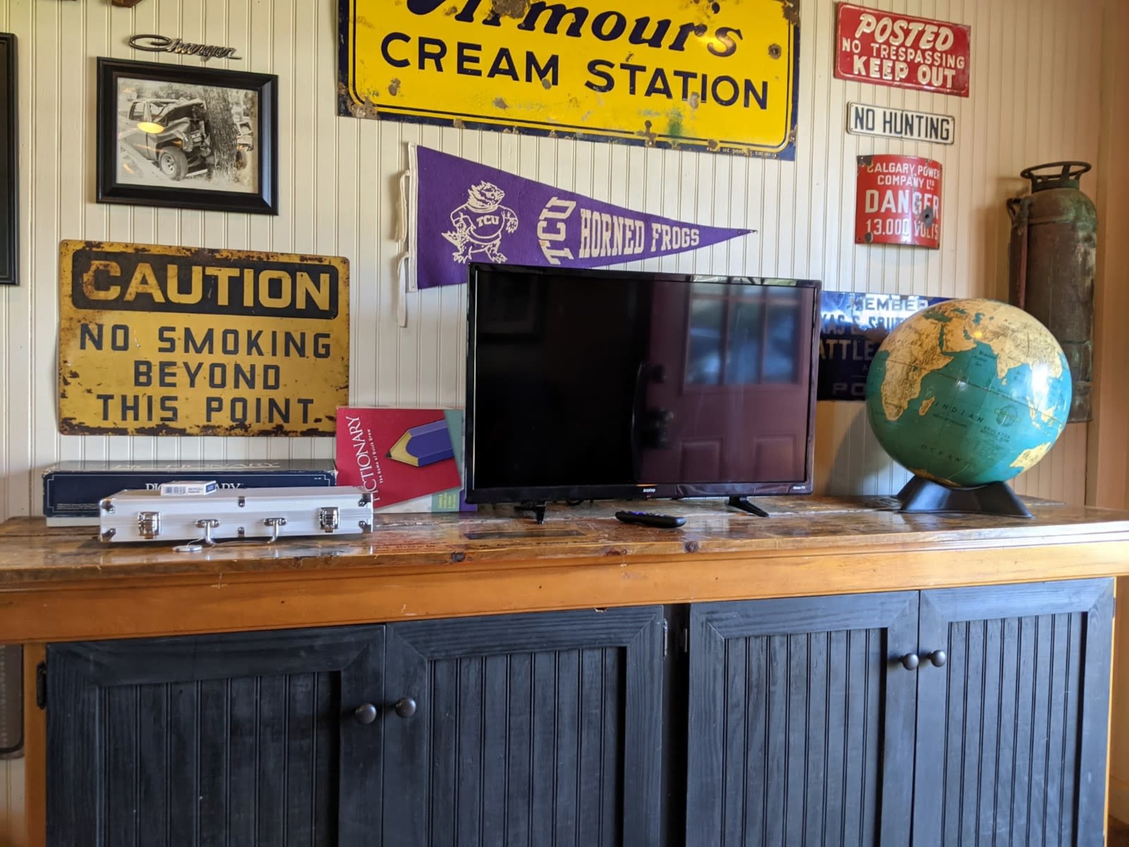 A wooden table with a television, a globe, and various signs including a caution sign and an old-fashioned advertising sign, all set in a room with wooden paneling.