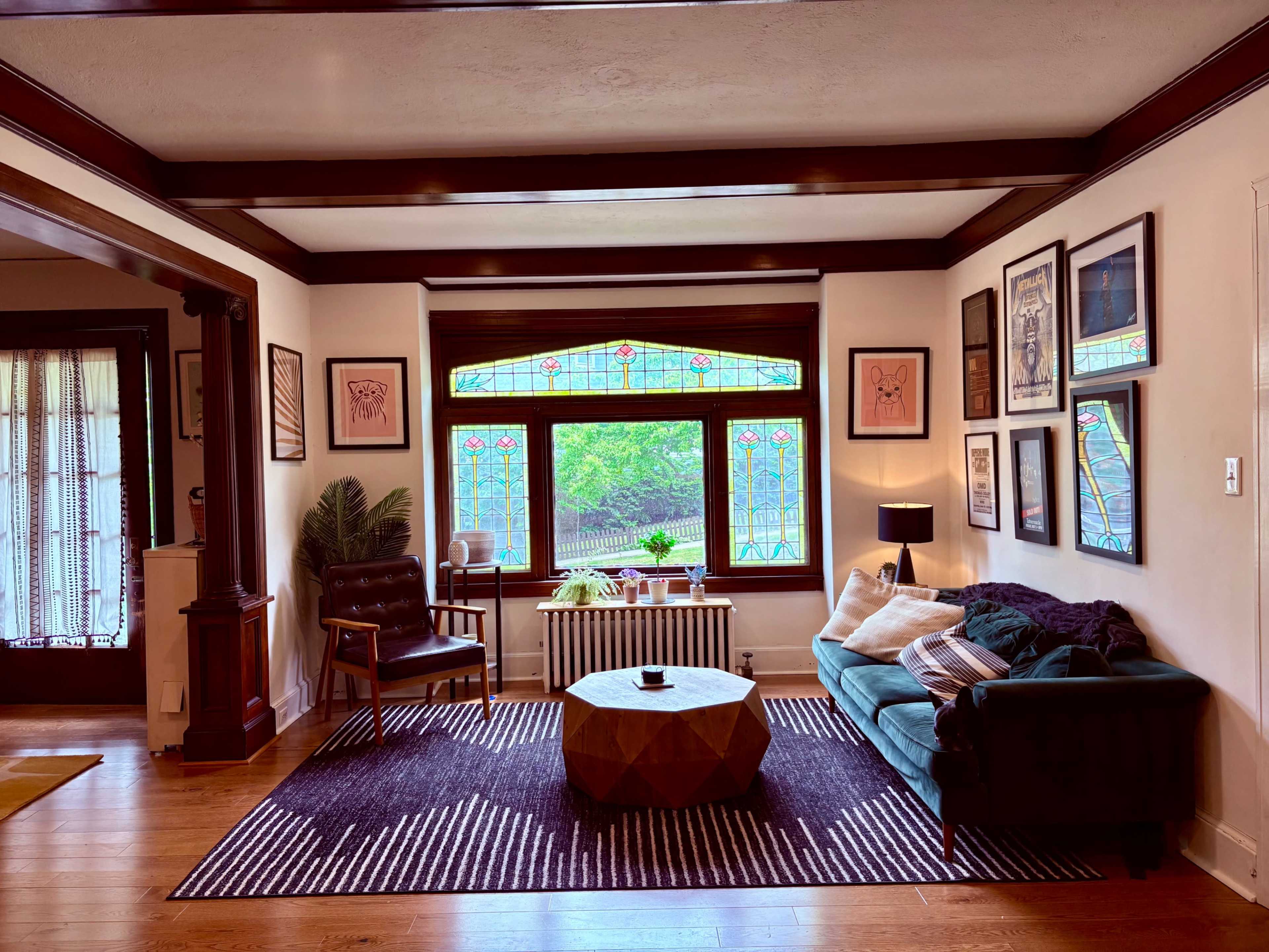 The living room features a green sofa, a geometric coffee table, and a large stained glass window surrounded by framed artwork.