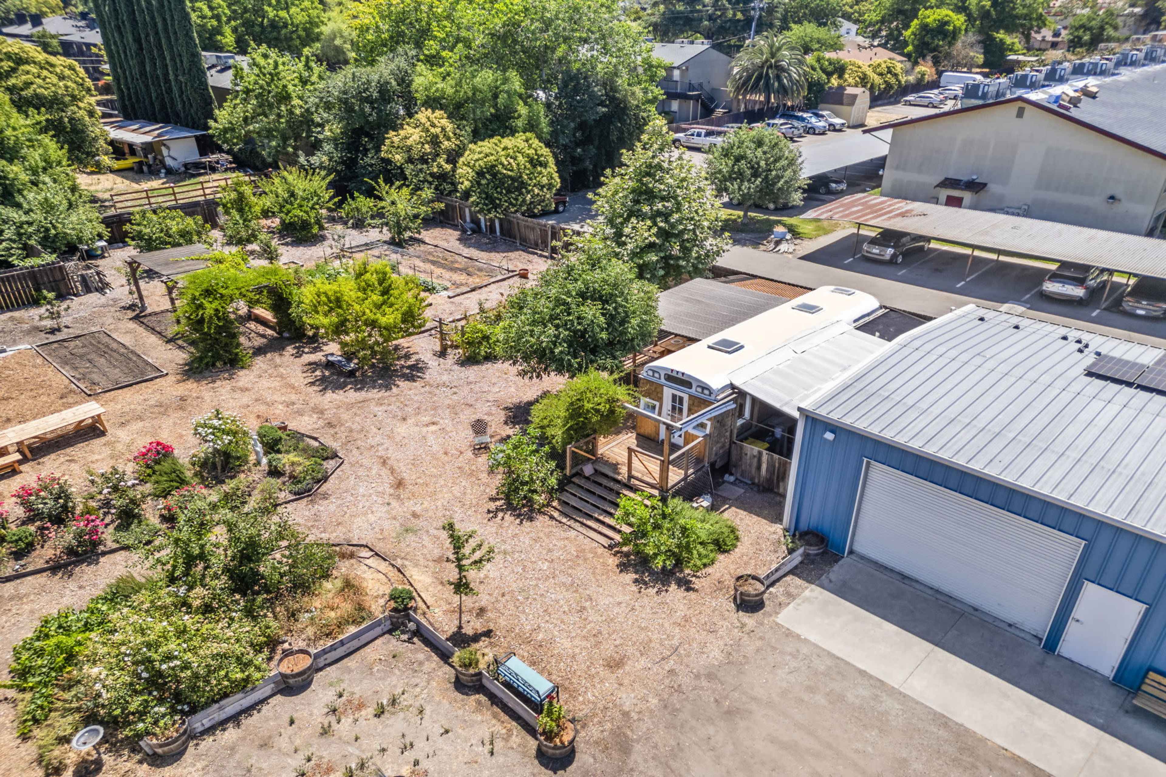 An aerial view of a landscaped garden area with walking paths, various plants, and a small structure beside a larger building.