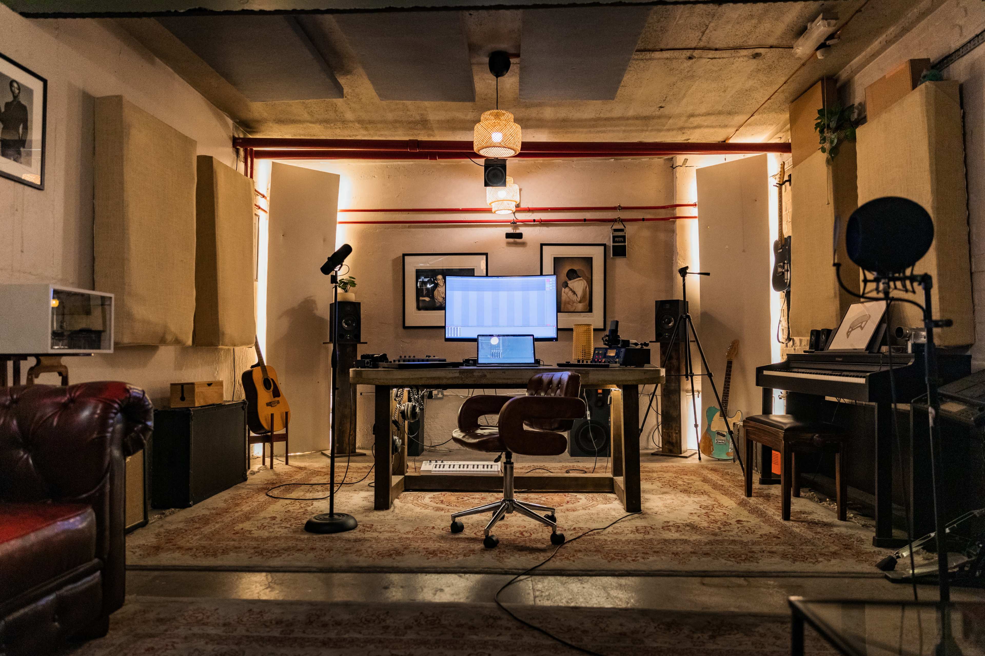 The image shows a recording studio with a central desk featuring a computer, surrounded by musical instruments and sound equipment.