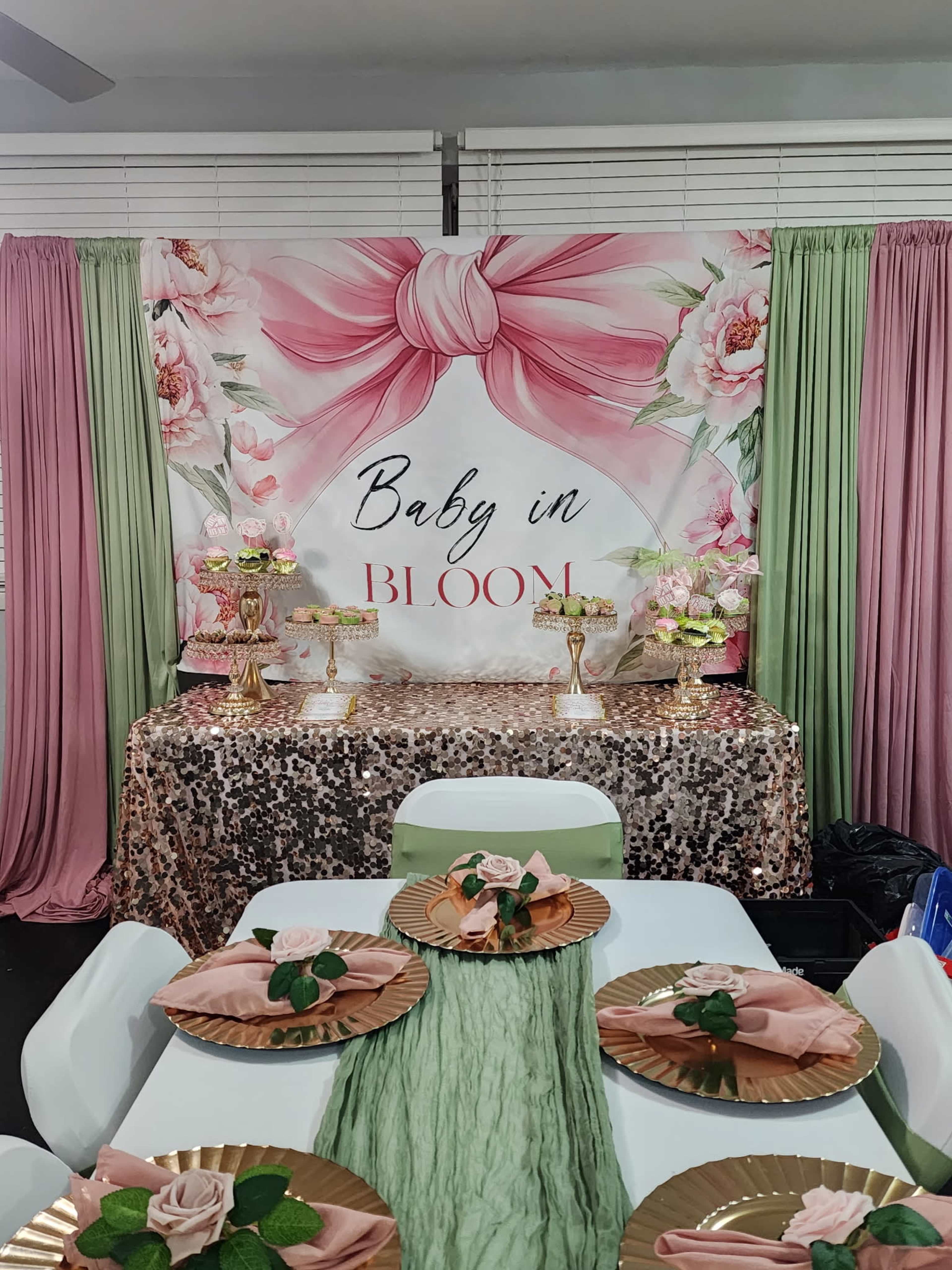 The image shows a decorated table for a baby shower, featuring a floral backdrop, gold decorations, and green and pink table settings.