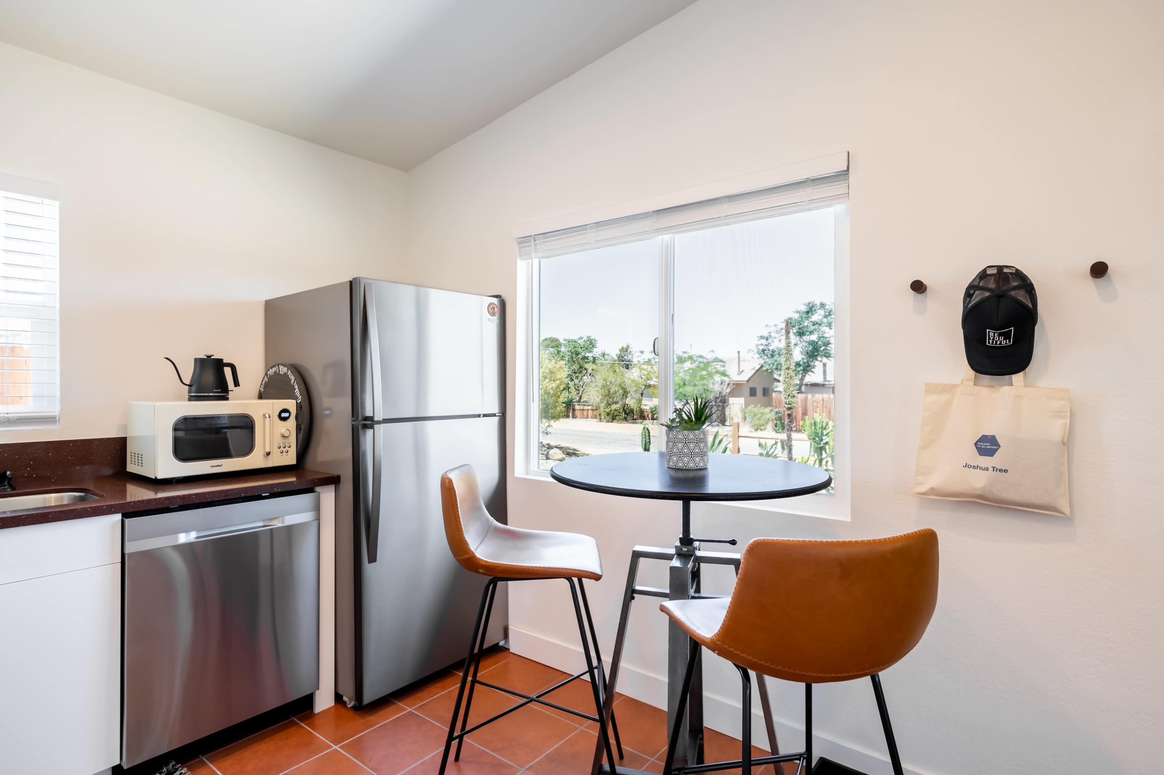 A modern kitchen features a stainless steel refrigerator, a microwave, and two brown bar stools at a round table by a window.