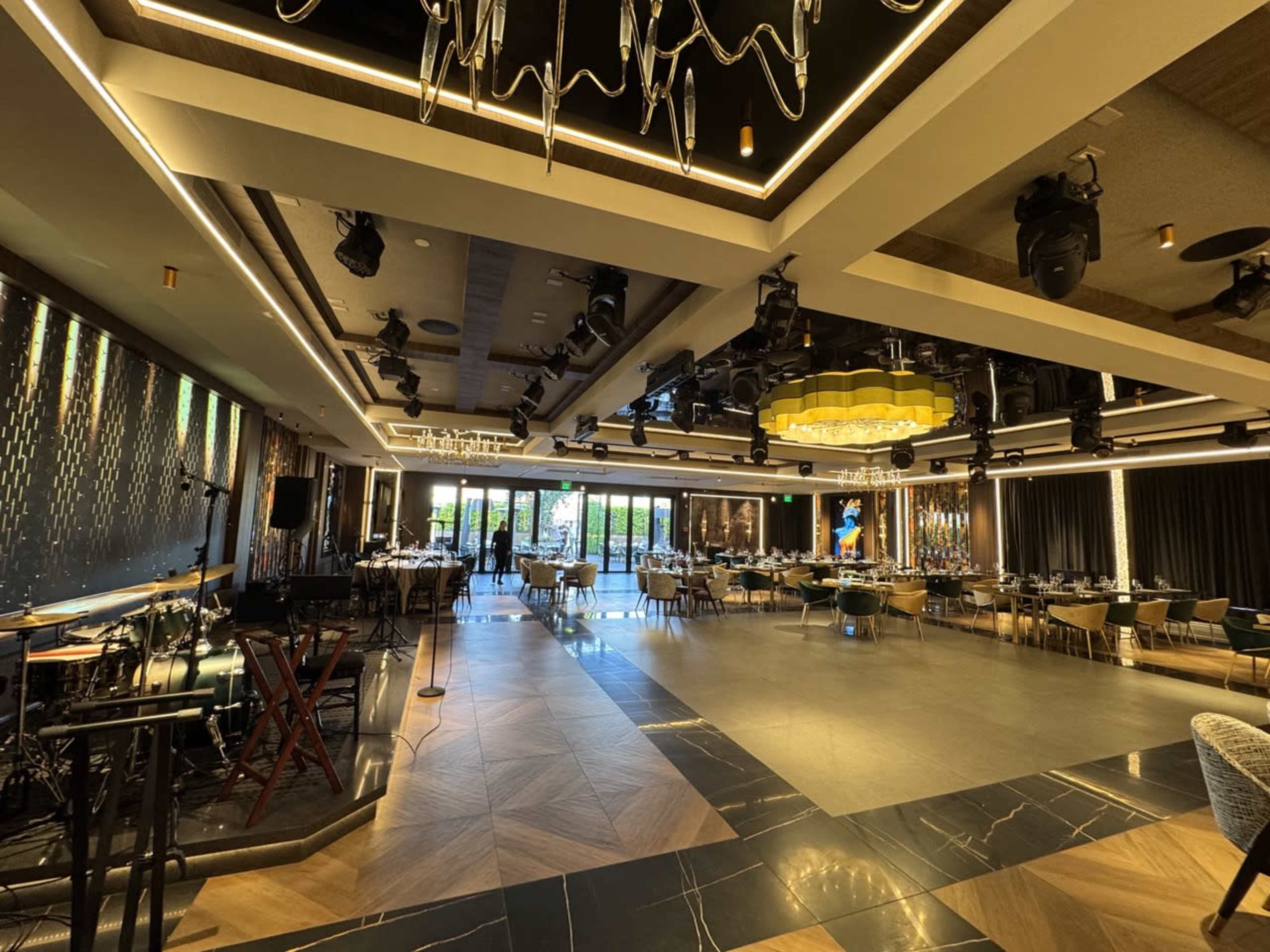 The image shows a spacious restaurant interior with modern lighting, elegantly set tables, and a stage area for performances.