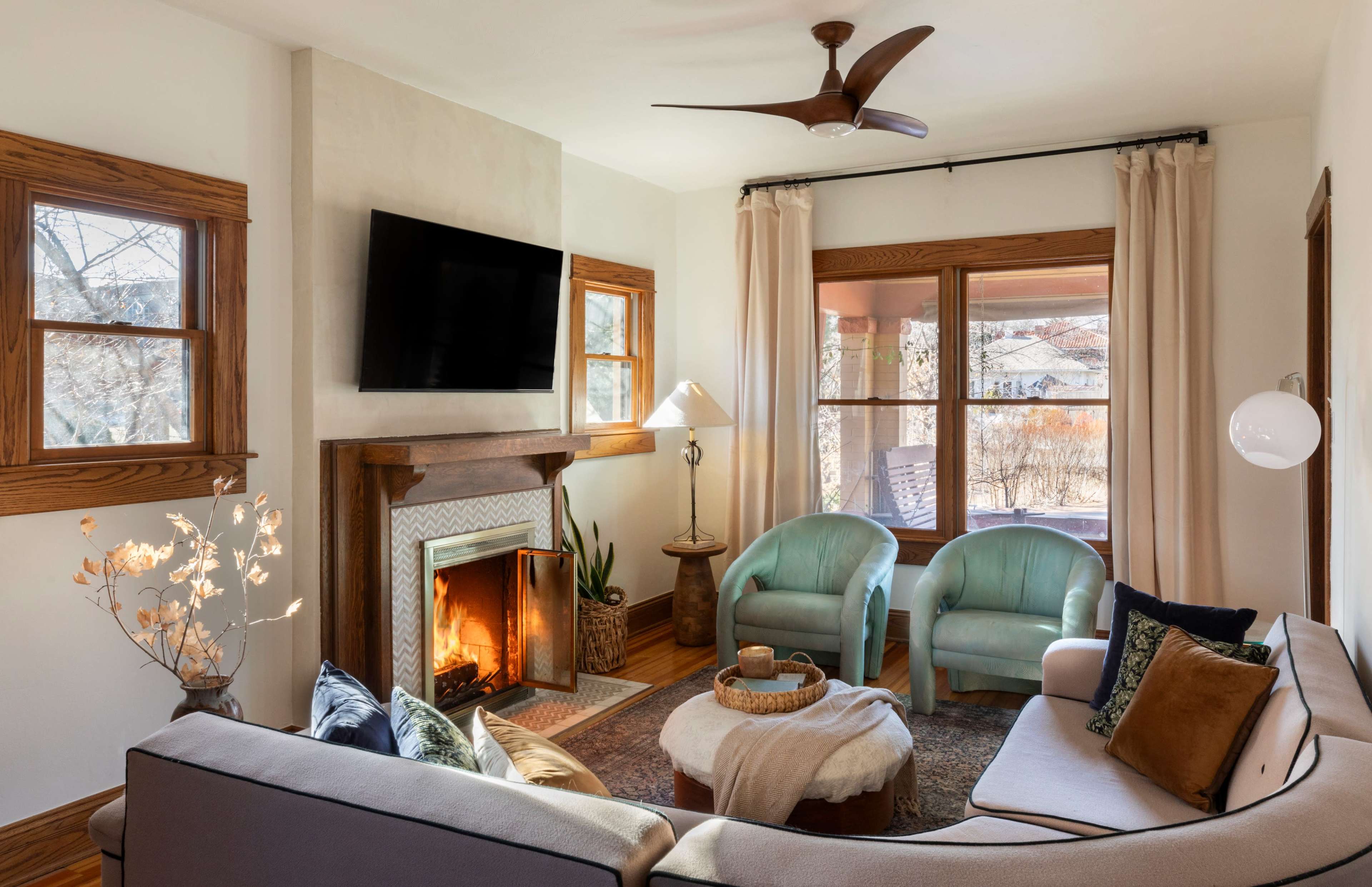 A cozy living room featuring a fireplace, two light blue chairs, a round coffee table, and large windows with natural light.