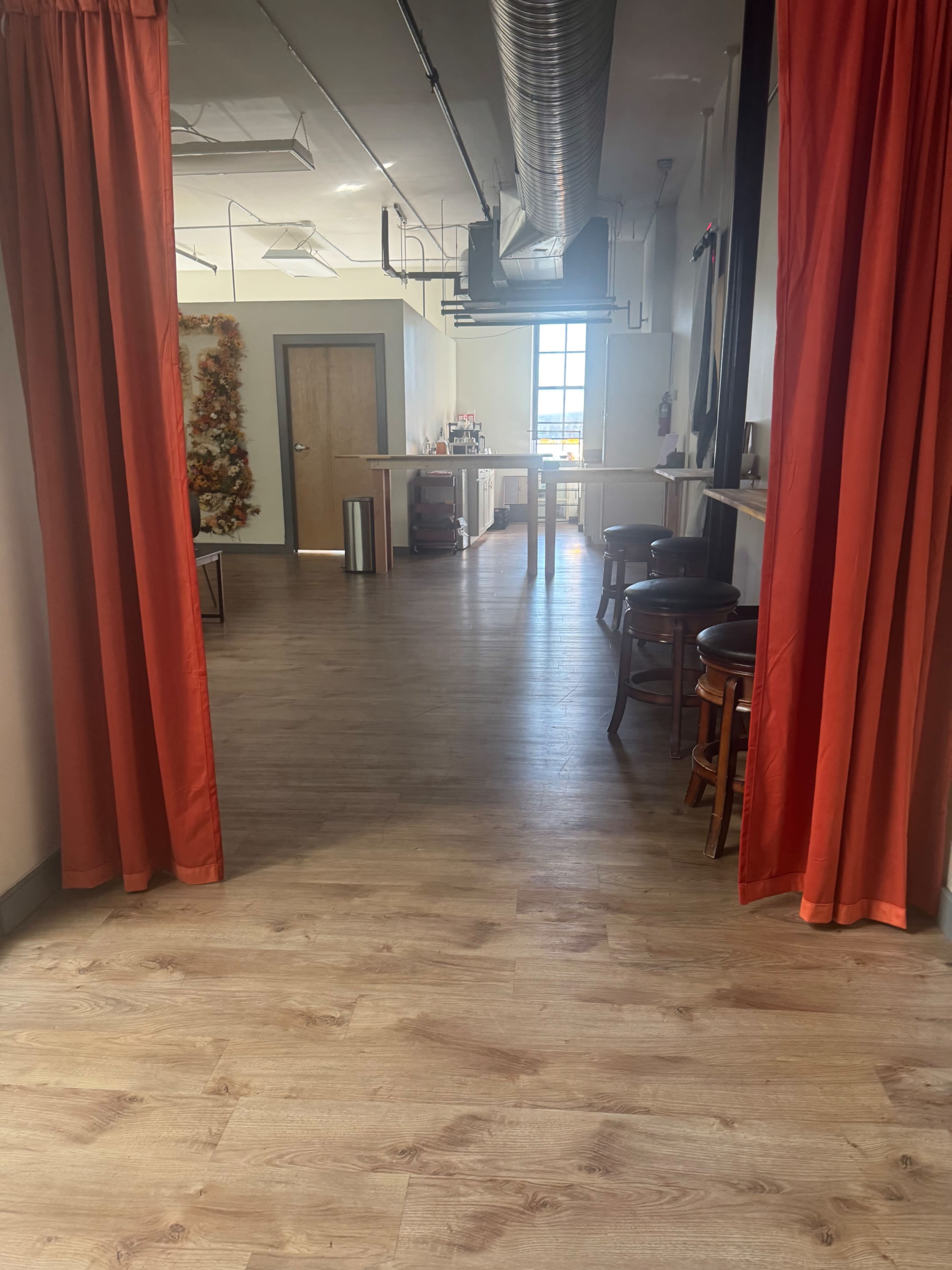 The image shows a spacious interior with wooden flooring, orange curtains framing an entrance to a room that features a bar area and large windows.