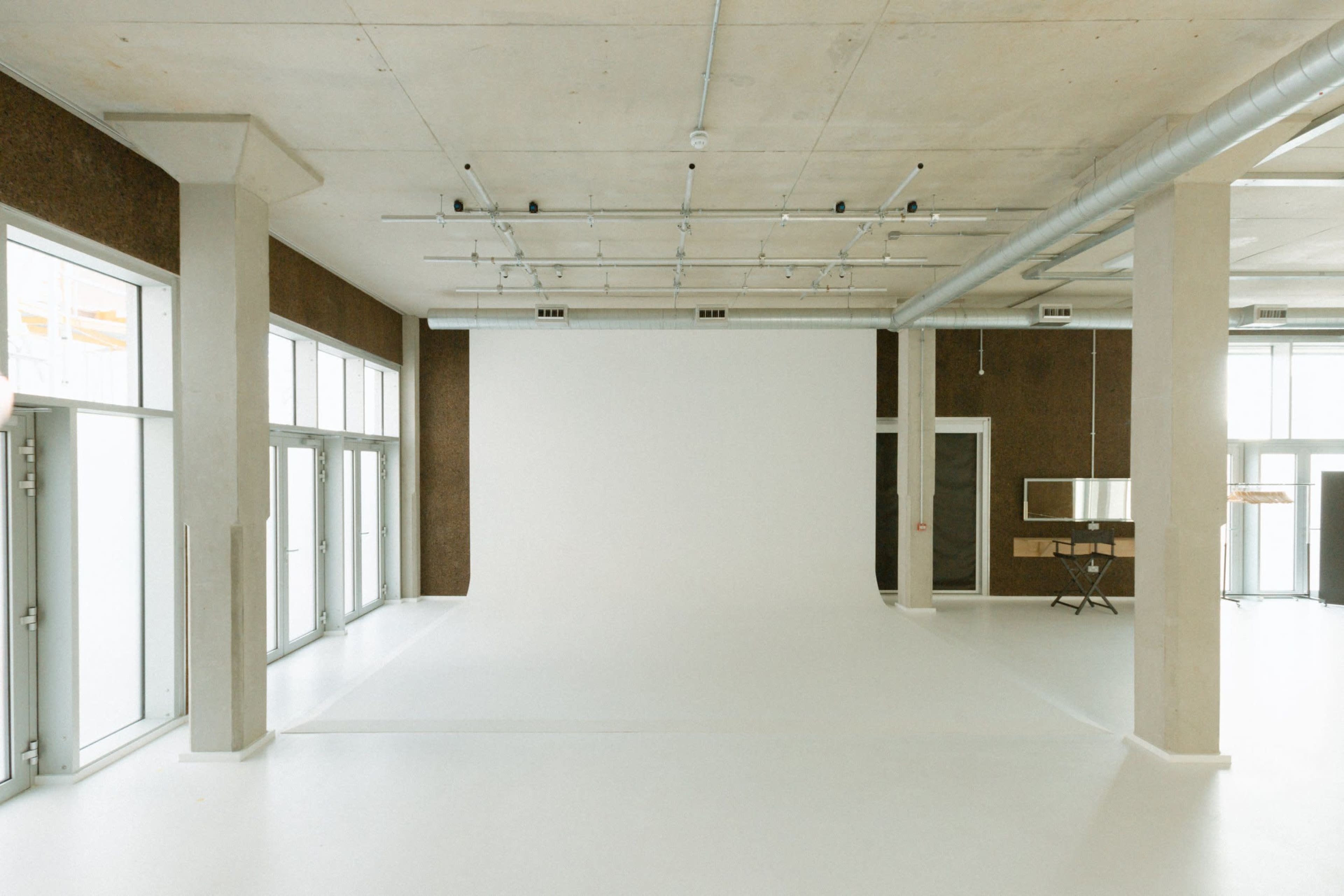A spacious, empty studio with a white backdrop, large windows, and visible industrial features.