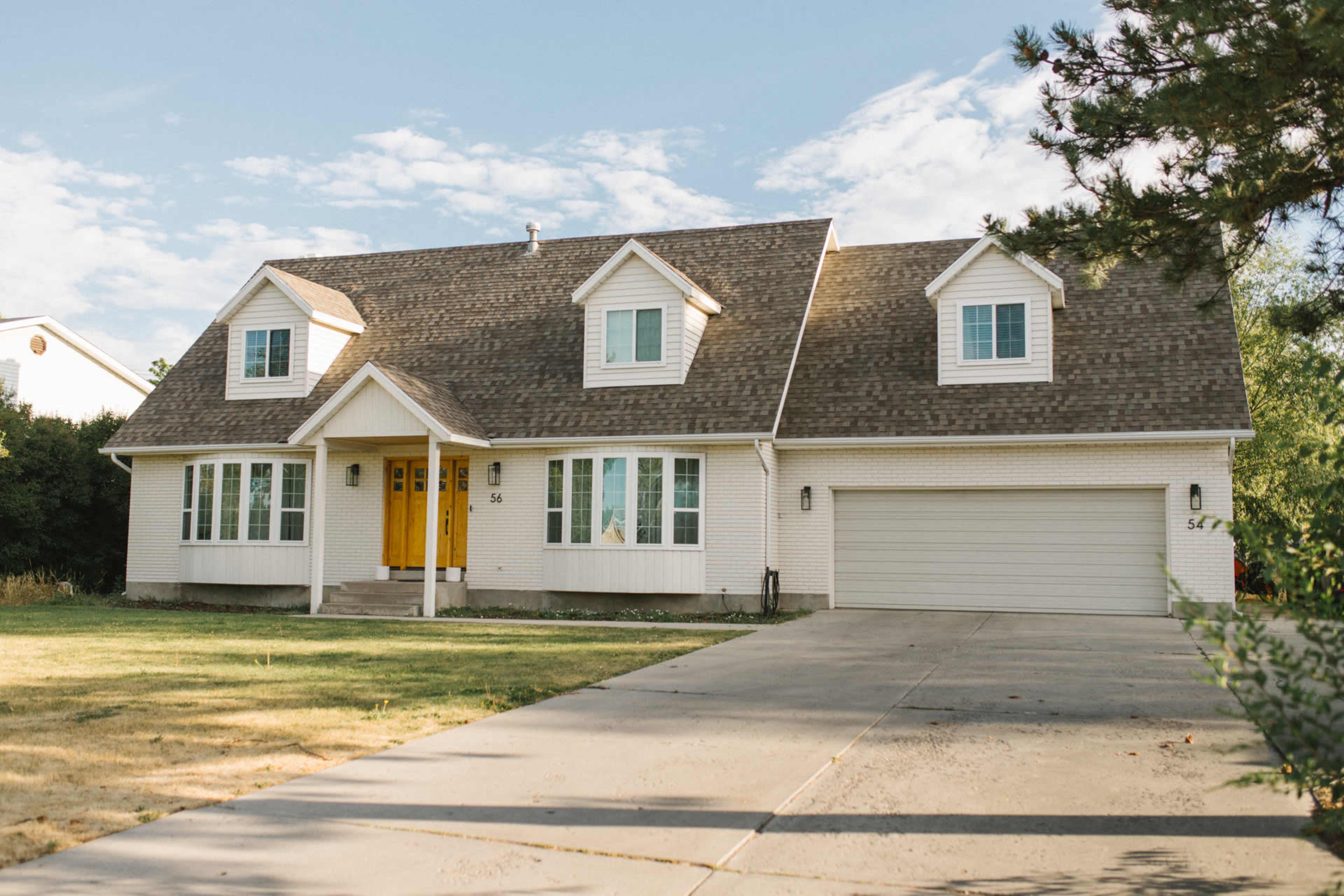 A large, two-story house with a front porch and a double garage is situated on a grassy lot under a partly cloudy sky.