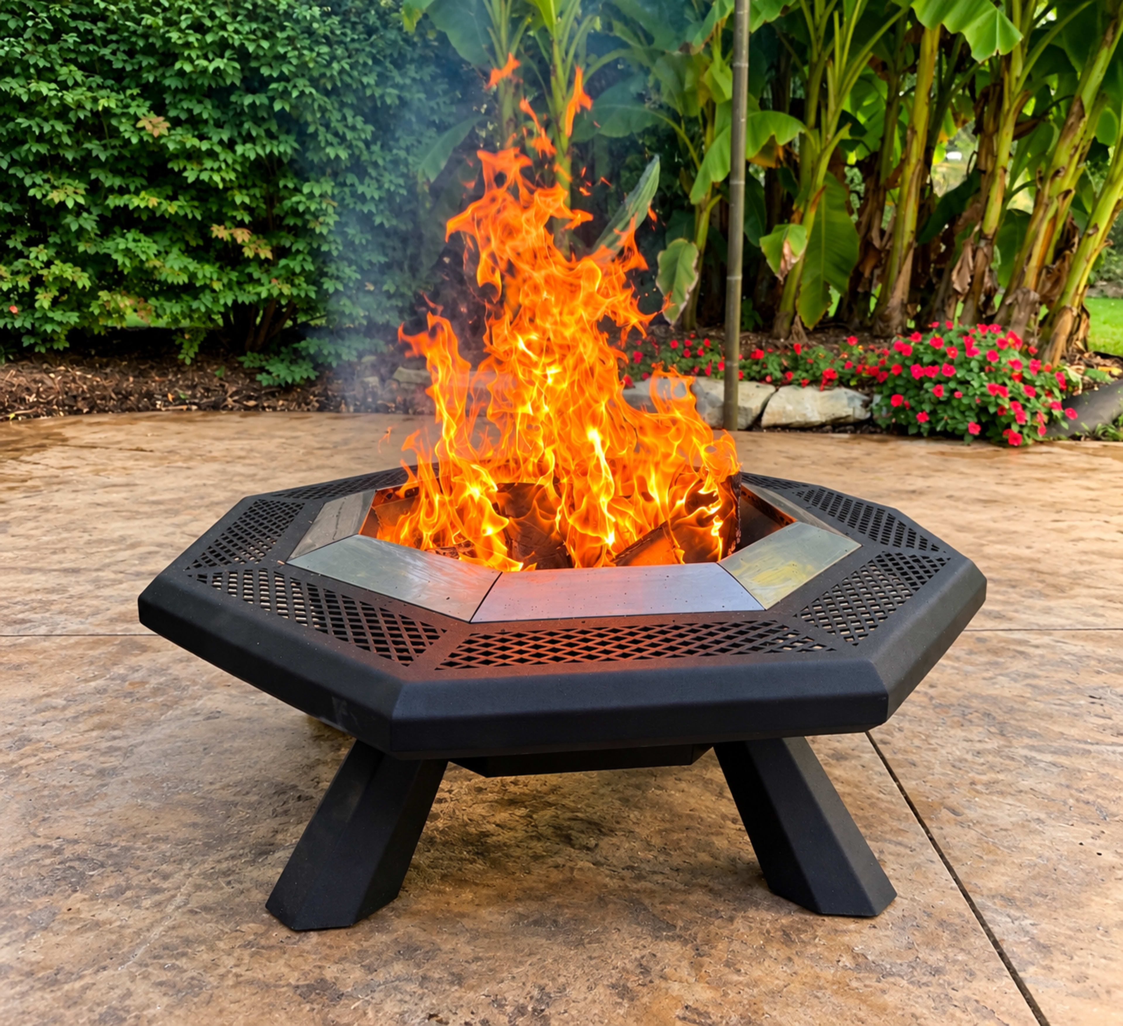 A metal fire pit with an octagonal design emits bright flames in a landscaped backyard.