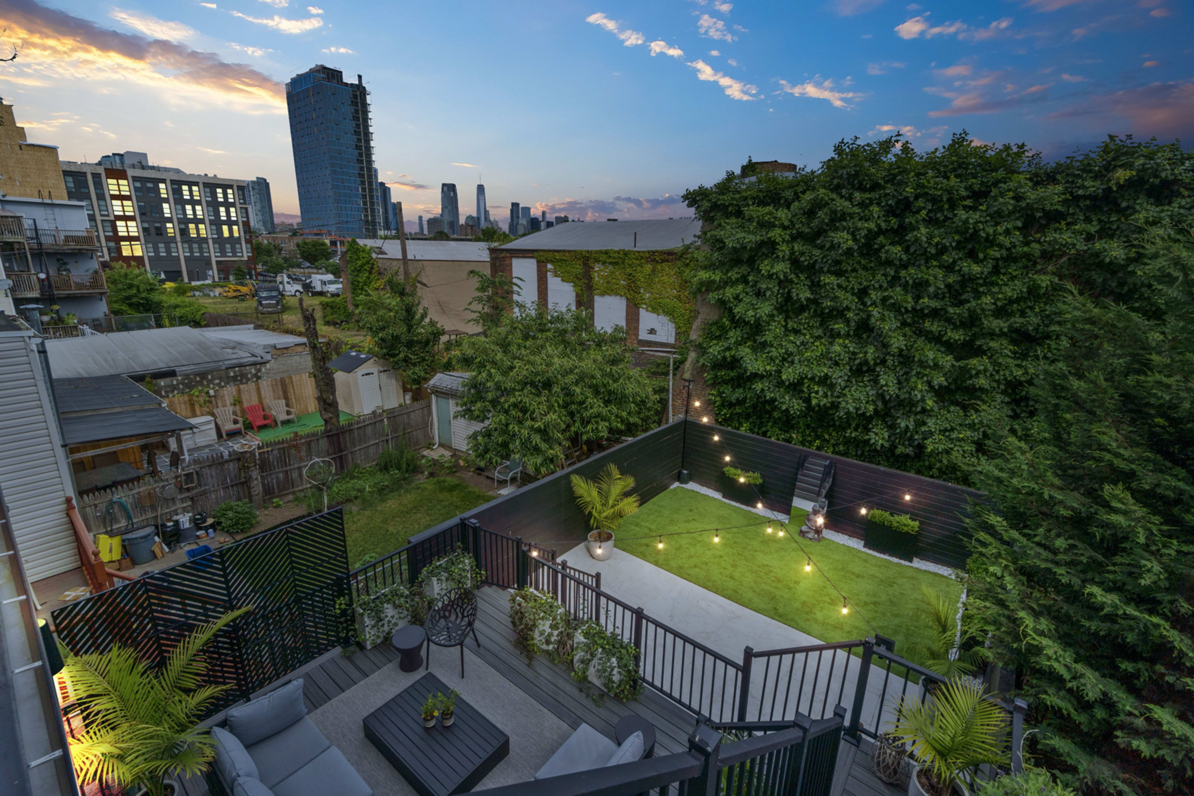 A rooftop garden with green grass, seating, and plants, overlooking a city skyline at dusk.